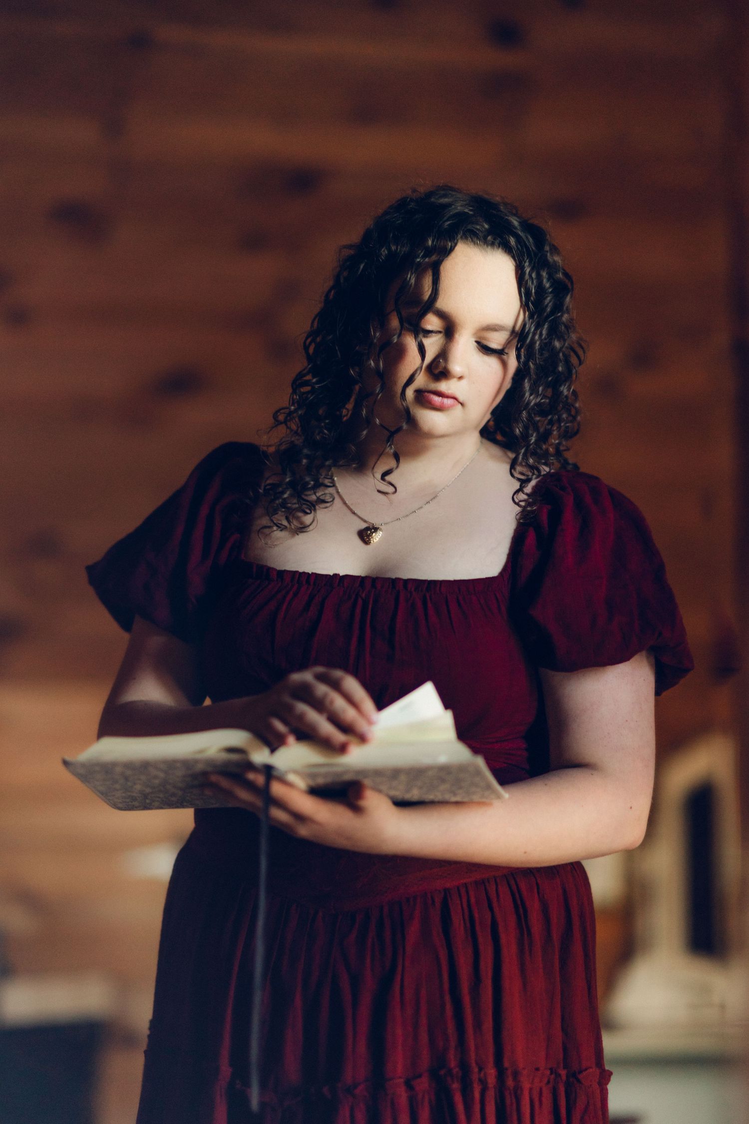 Young woman with curly hair in a red dress with her bible in a rustic wooden interior.
