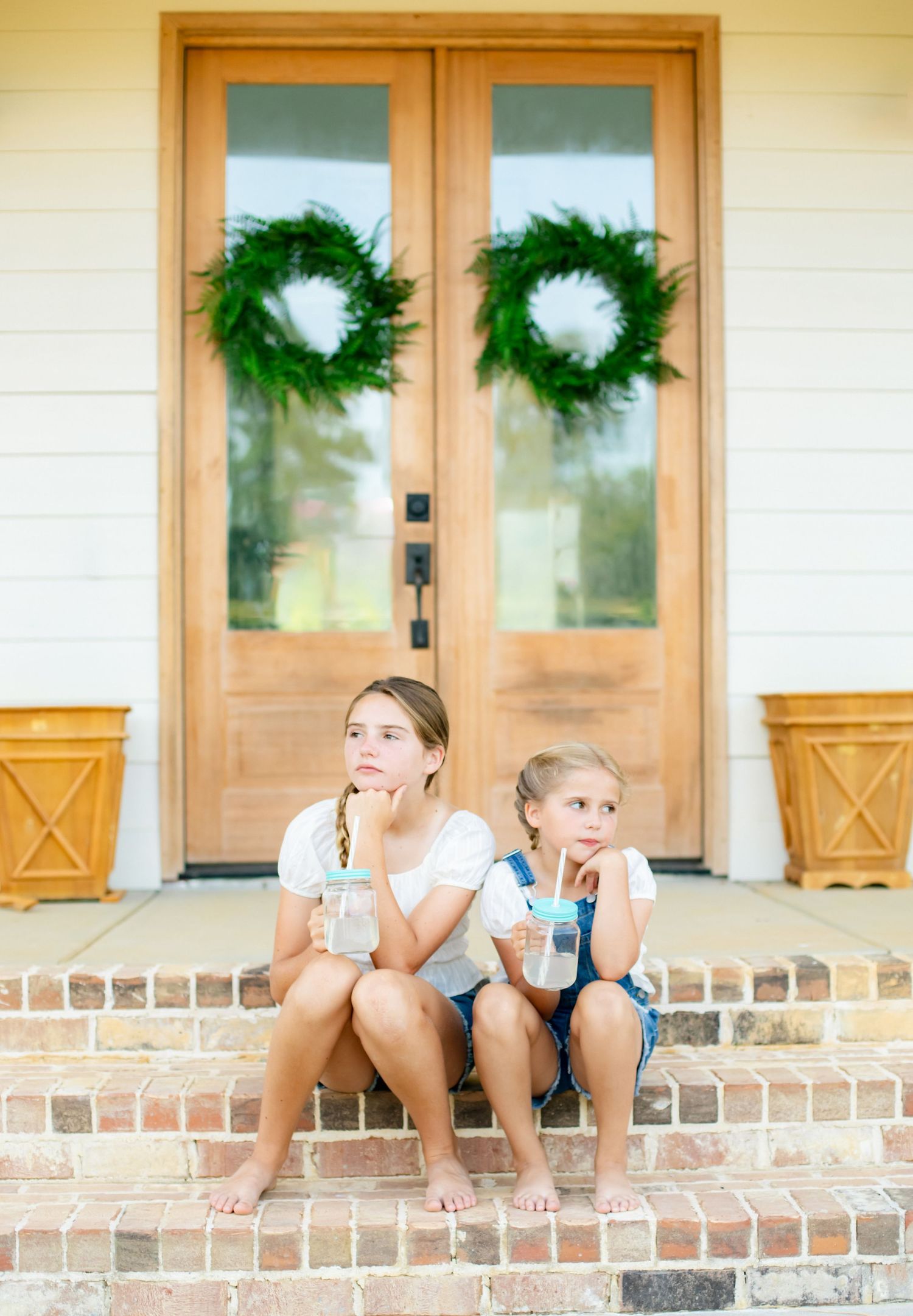 Sisters on the front steps of their home with wreaths on the door.