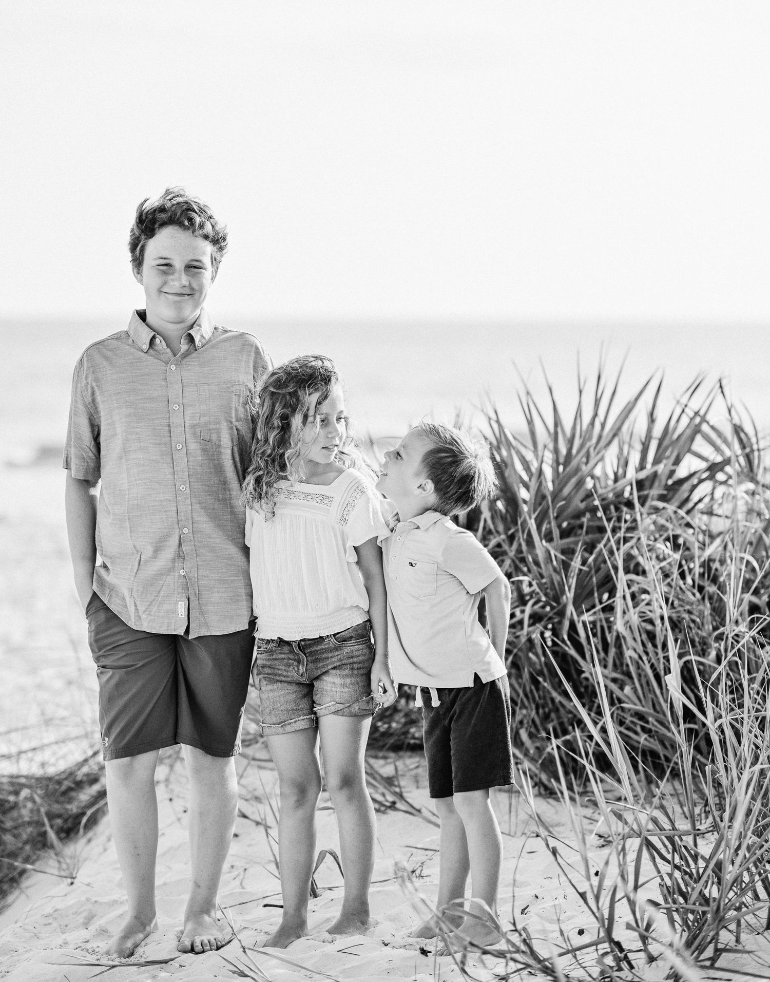 Kids on the beach in front of tall grass in black and white.