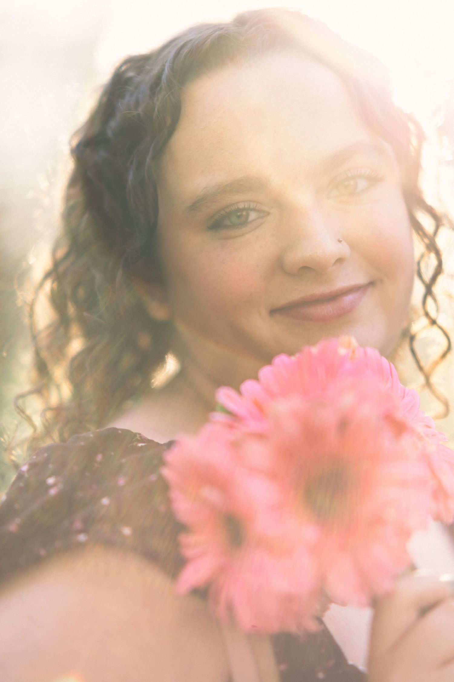 Ashlyn smiling softly while holding pink gerbera daisies in warm golden sunlight.