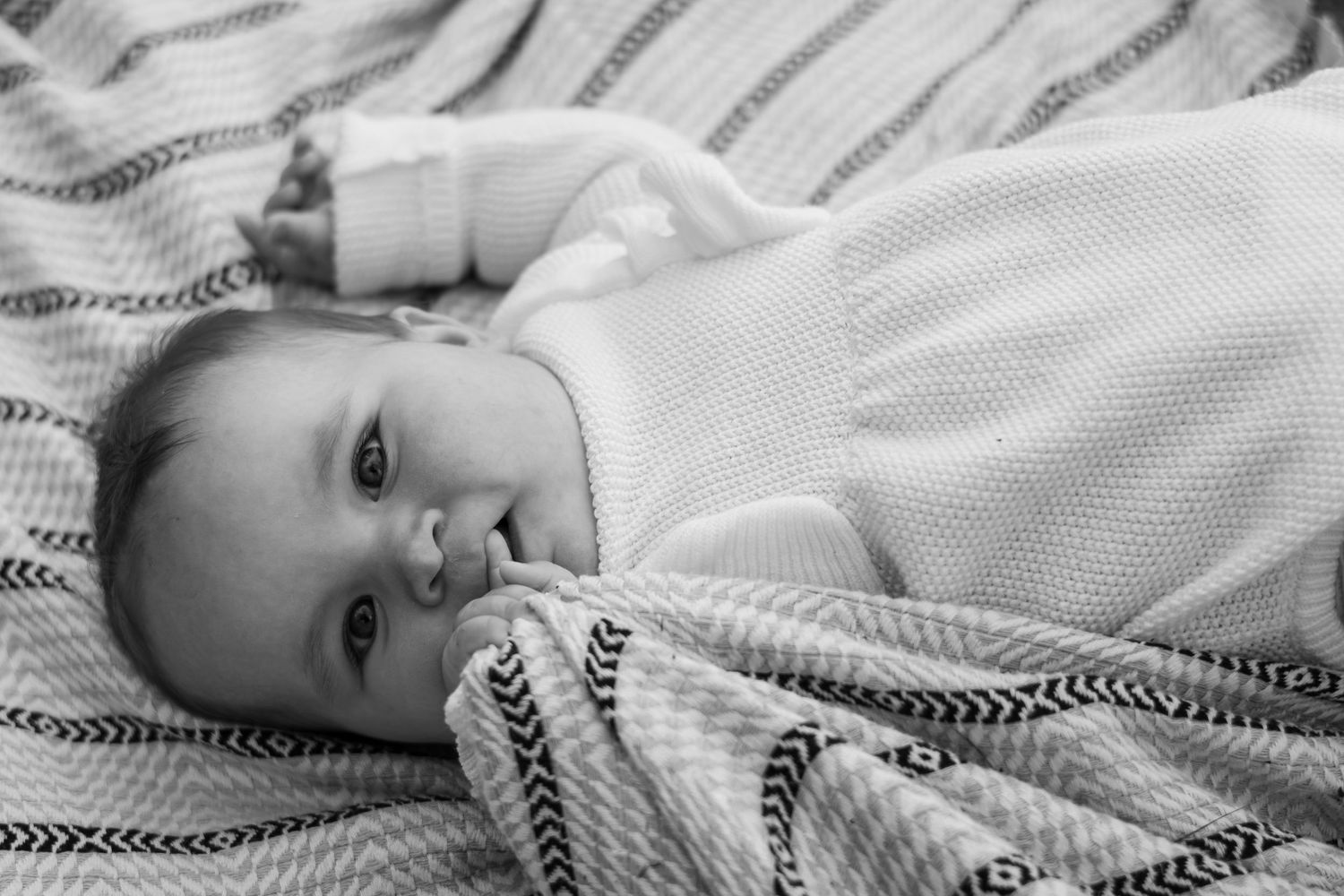 Black and white portrait of baby lying on striped blanket.