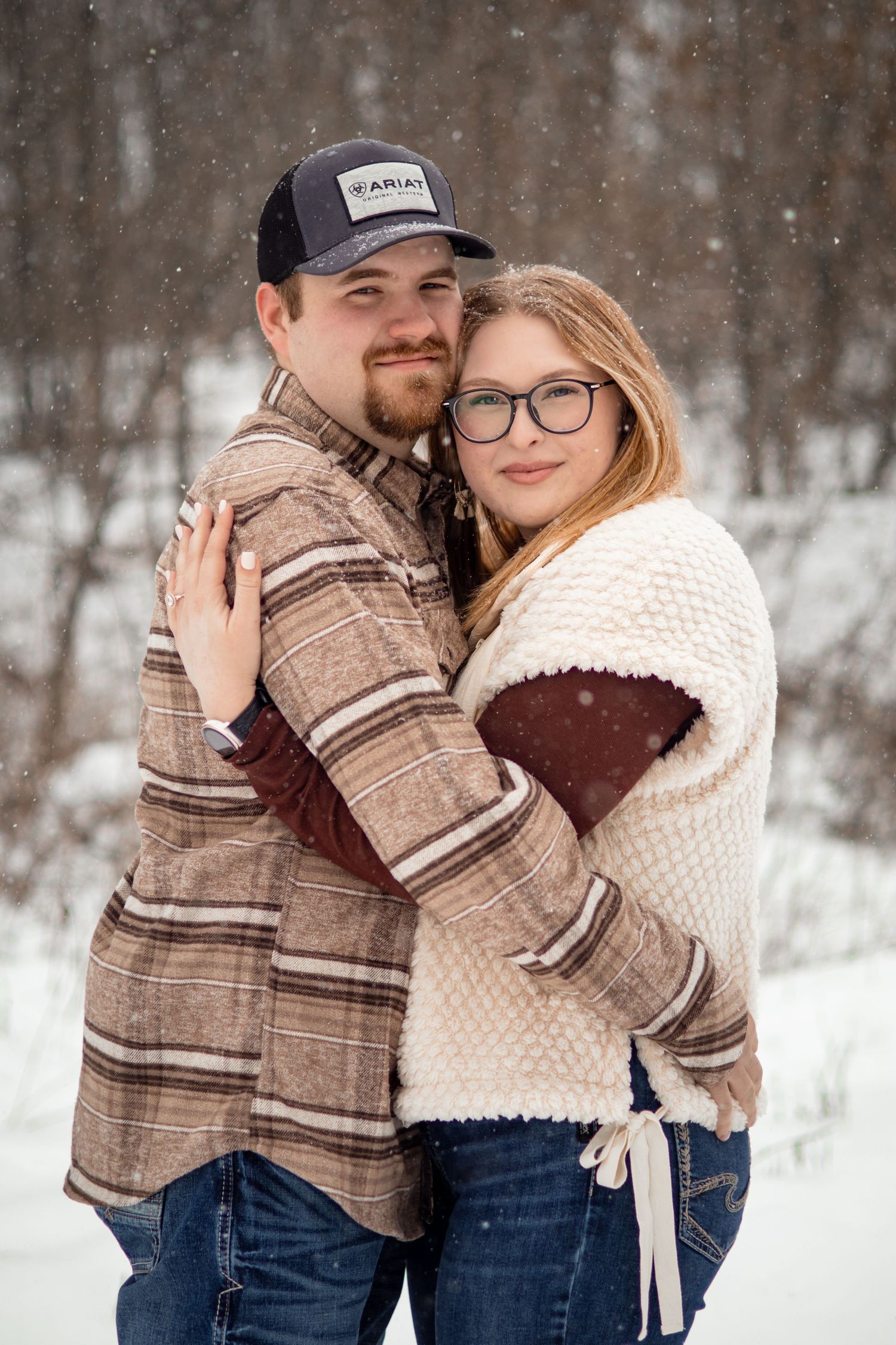 Romantic winter engagement photos with a couple in plaid and knit sweaters against snowy backdrop.