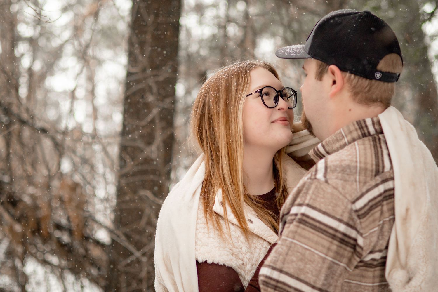 An intimate winter engagement photo among snow-covered trees.