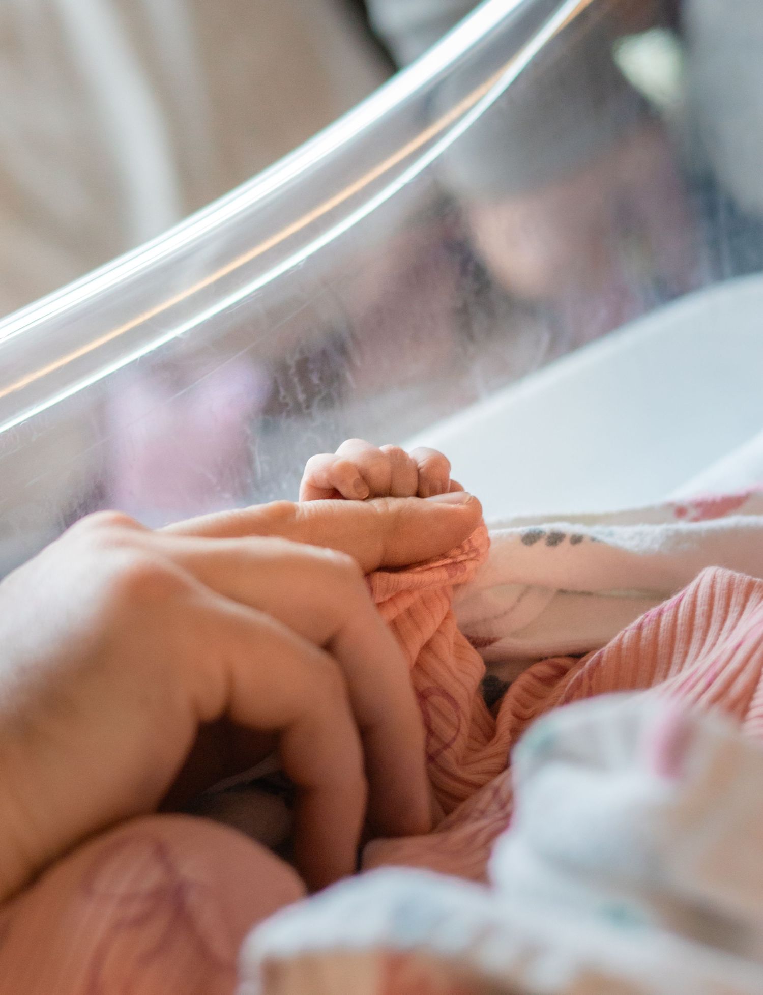 Close-up of gentle hand holding in hospital setting with medical equipment visible.