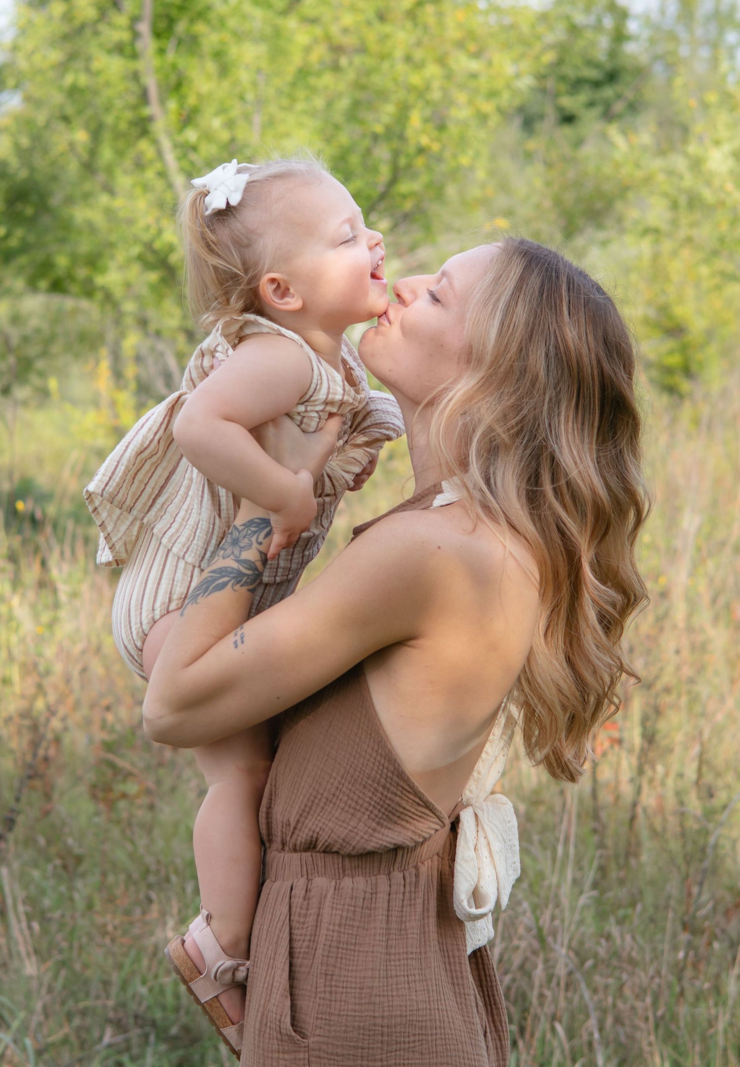 Mother and child sharing playful moments in a sun-lit field with natural grass backdrop.