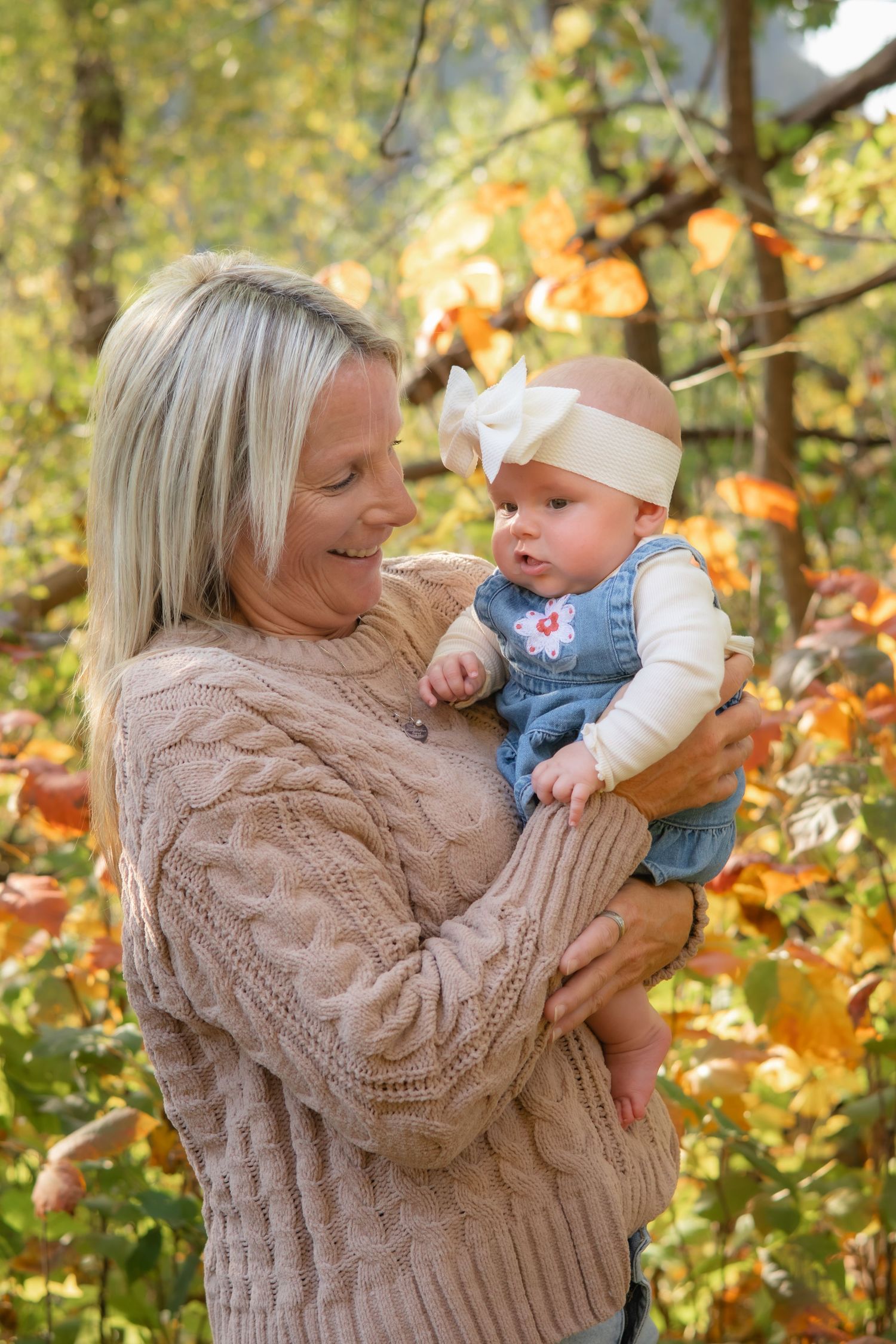 Person in beige cable knit sweater holding and playing with baby outdoors.