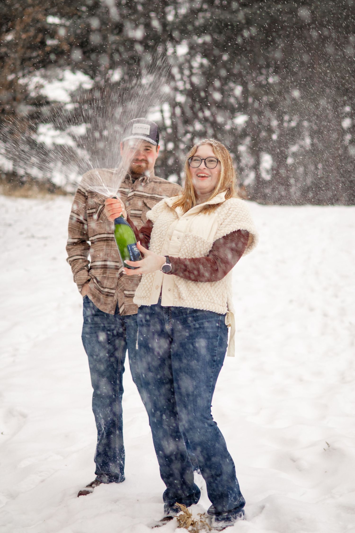 A playful couple throws snow during their winter engagement photoshoot.