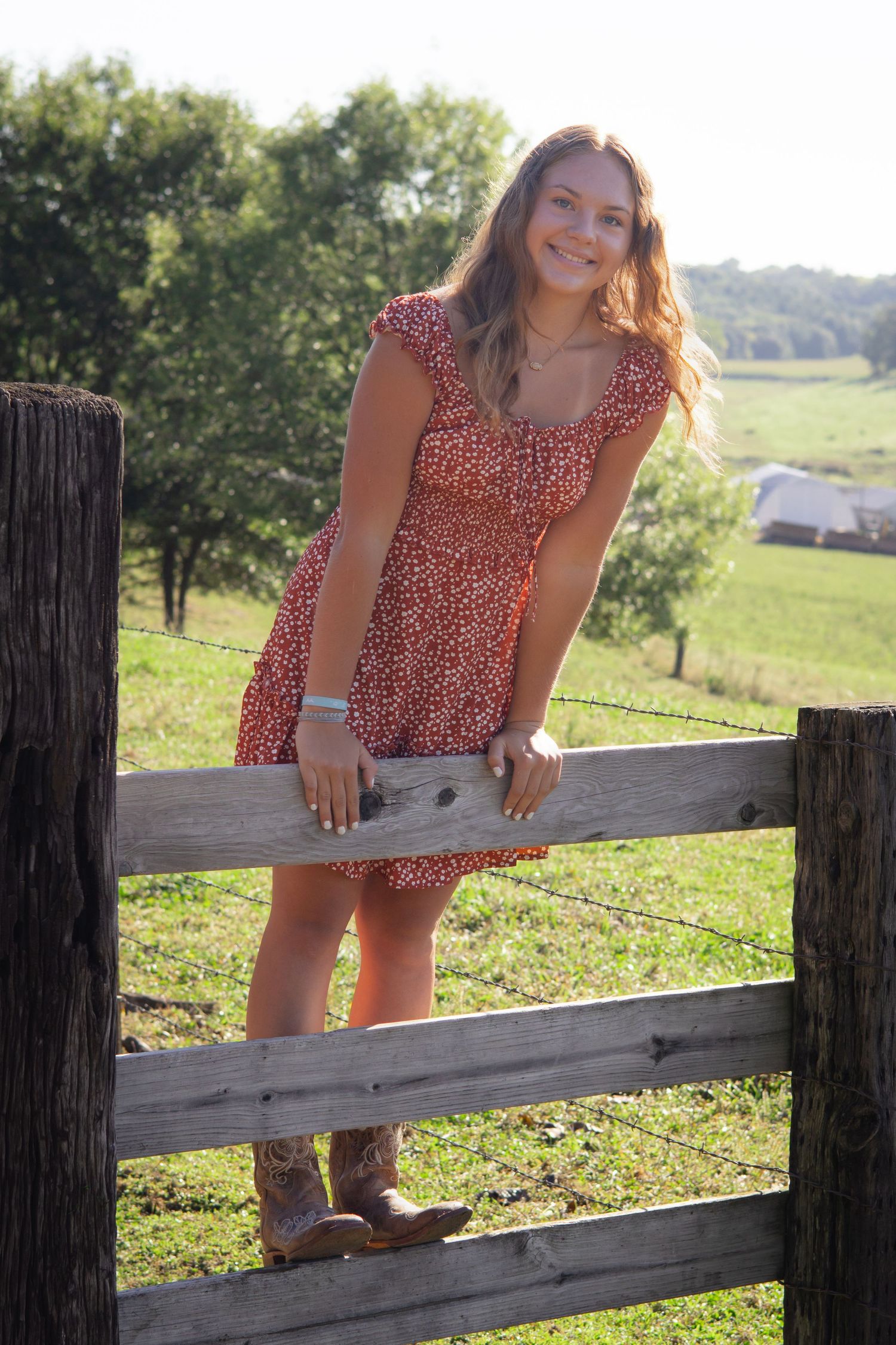 Woman in red polka dot dress posing by rustic wooden fence at sunset.