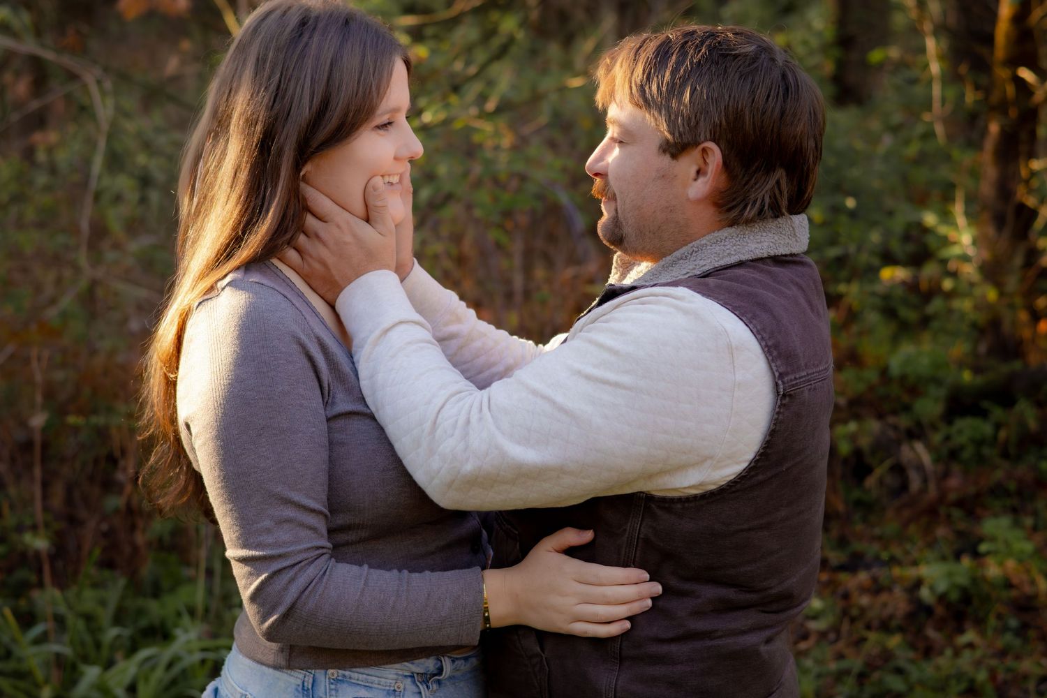 Romantic couple embracing in an autumn forest setting with golden sunlight filtering through trees.