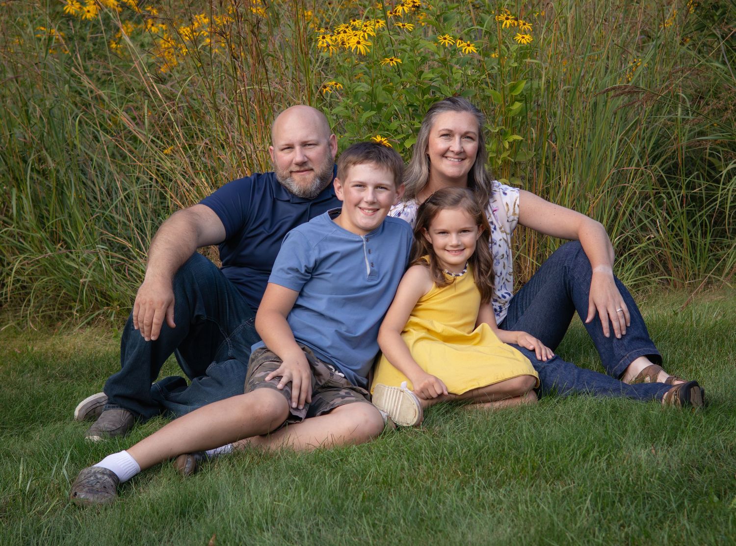 Family relaxing together on grass with yellow wildflowers in background.