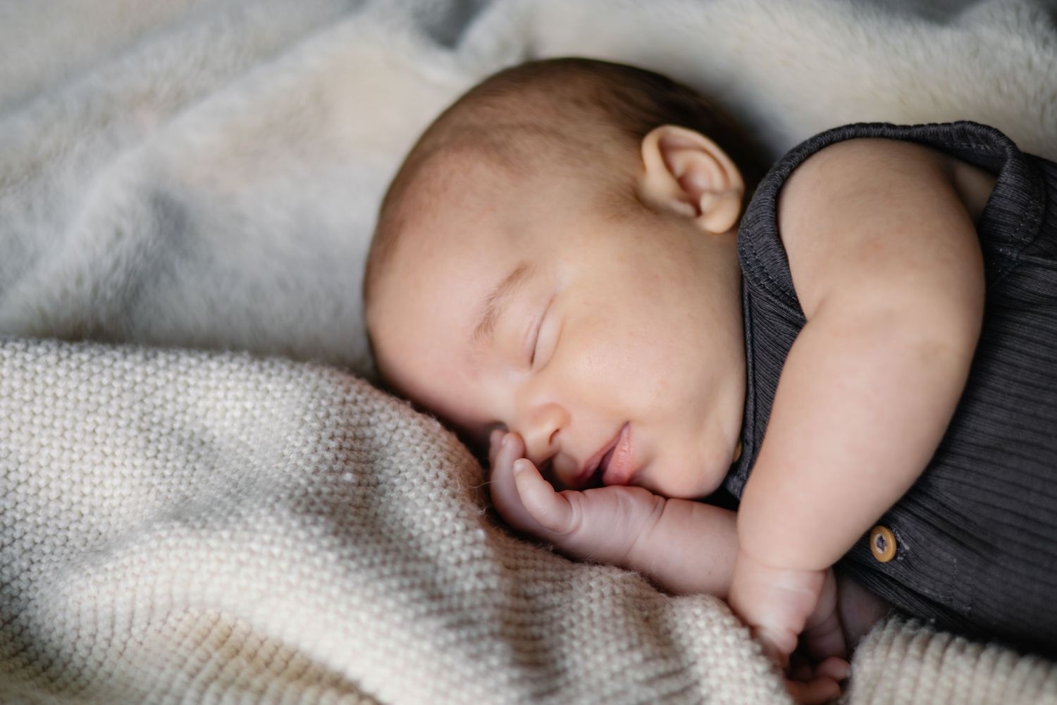 Peaceful sleeping infant in dark outfit on textured white blanket.