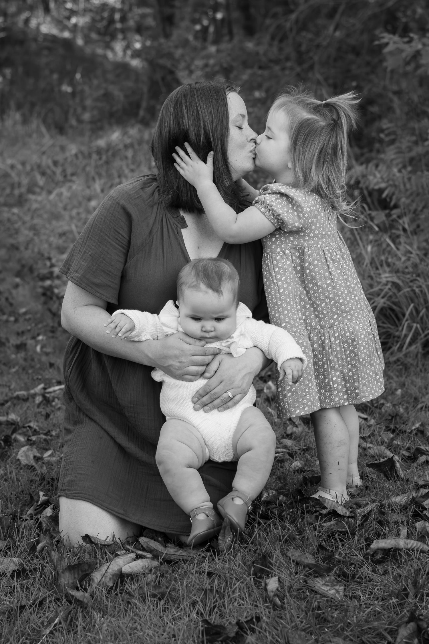 Family sharing intimate moments together on grass in black and white portrait.
