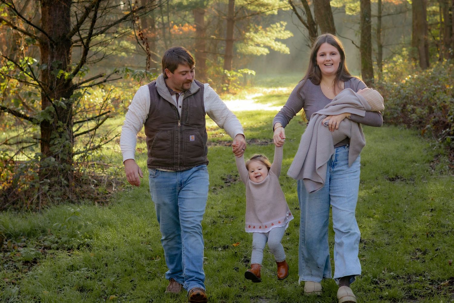 Family enjoying a playful moment together in a sunlit forest setting.