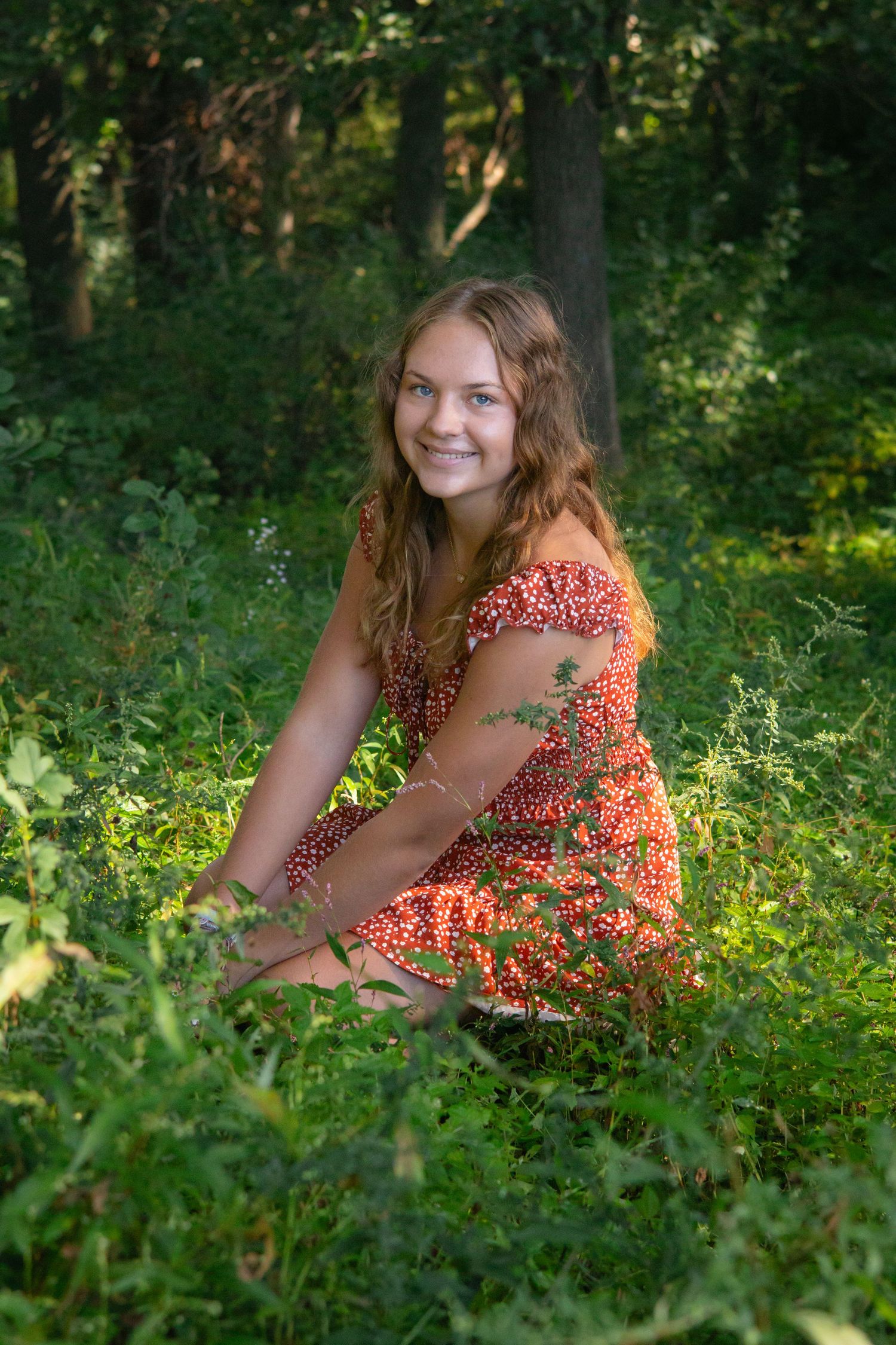 Summer portrait session in lush green grass wearing a floral orange dress.