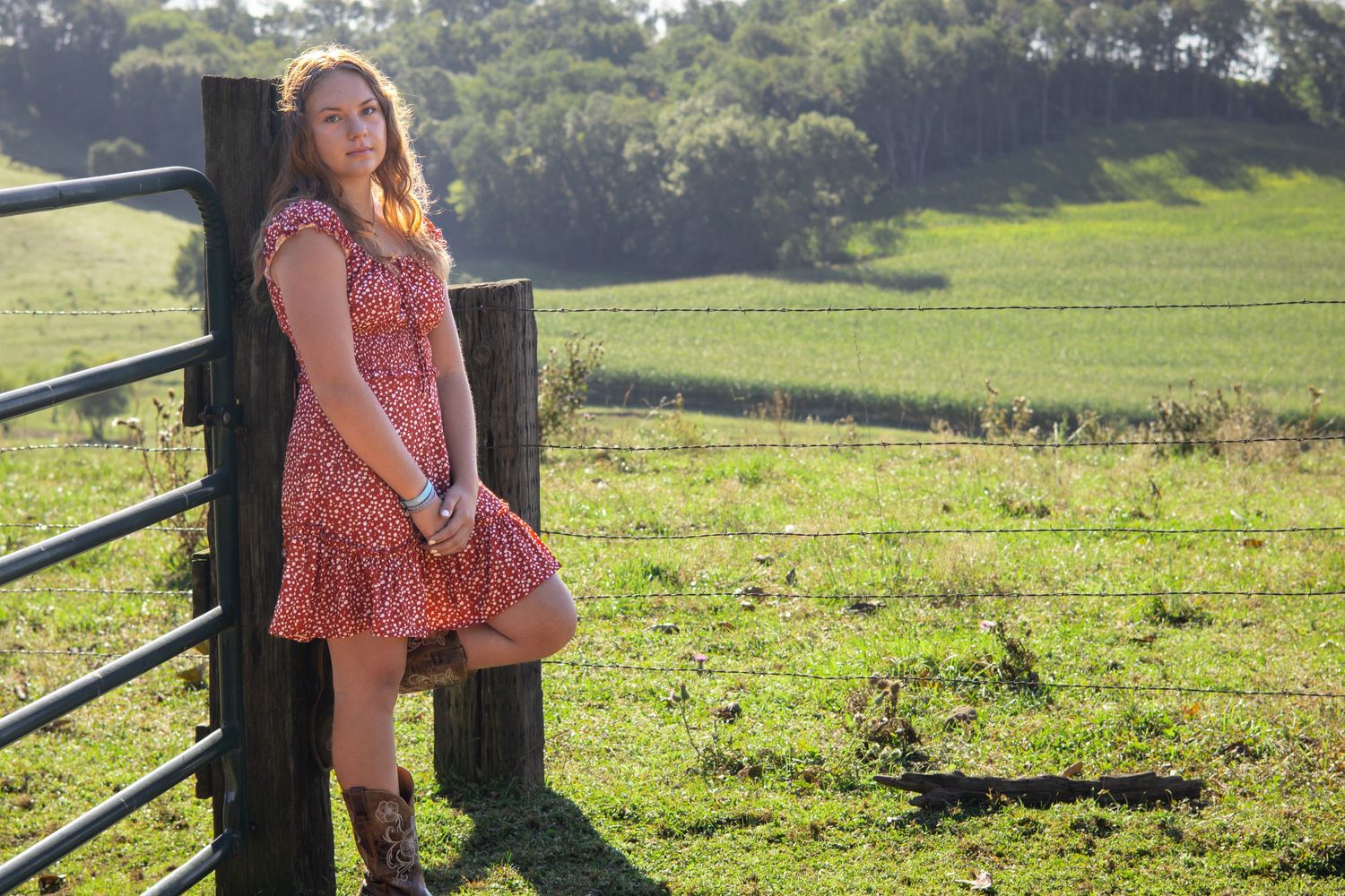 Rustic outdoor portrait in floral dress against wooden post with sunlit meadow.