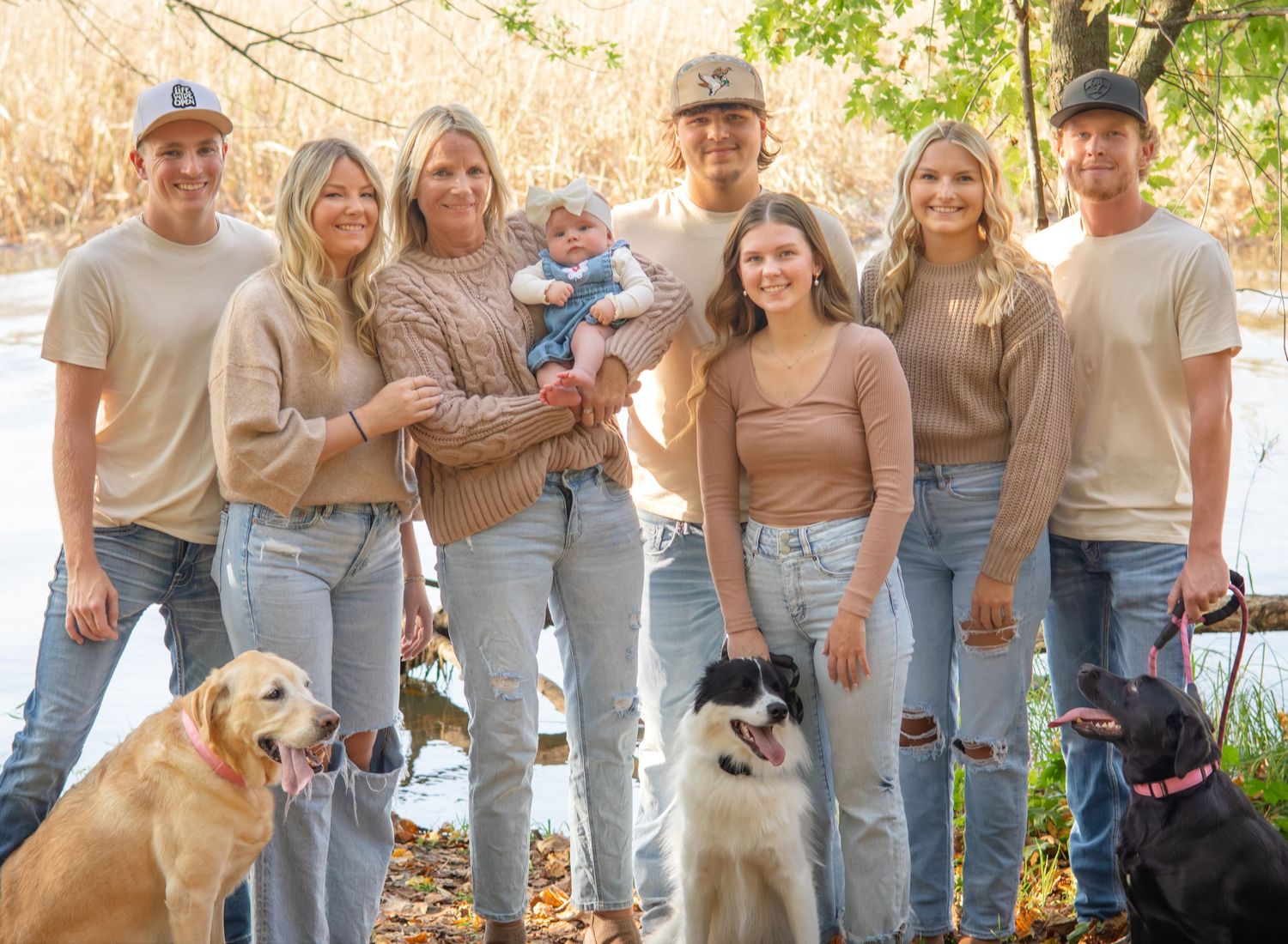 Extended family and dogs pose together outdoors wearing matching casual outfits with distressed jeans.