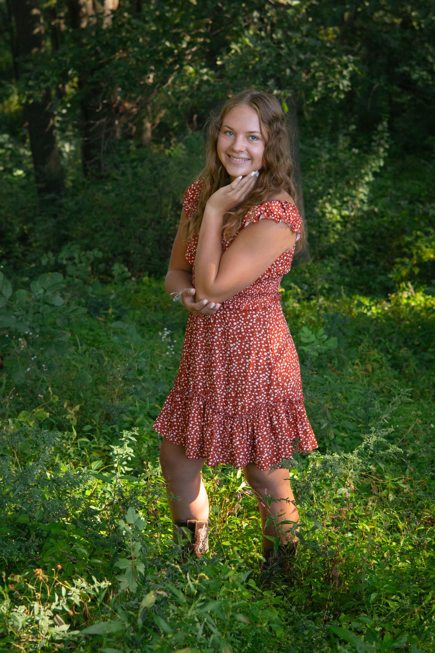 Person in red floral dress poses playfully in green summer forest.
