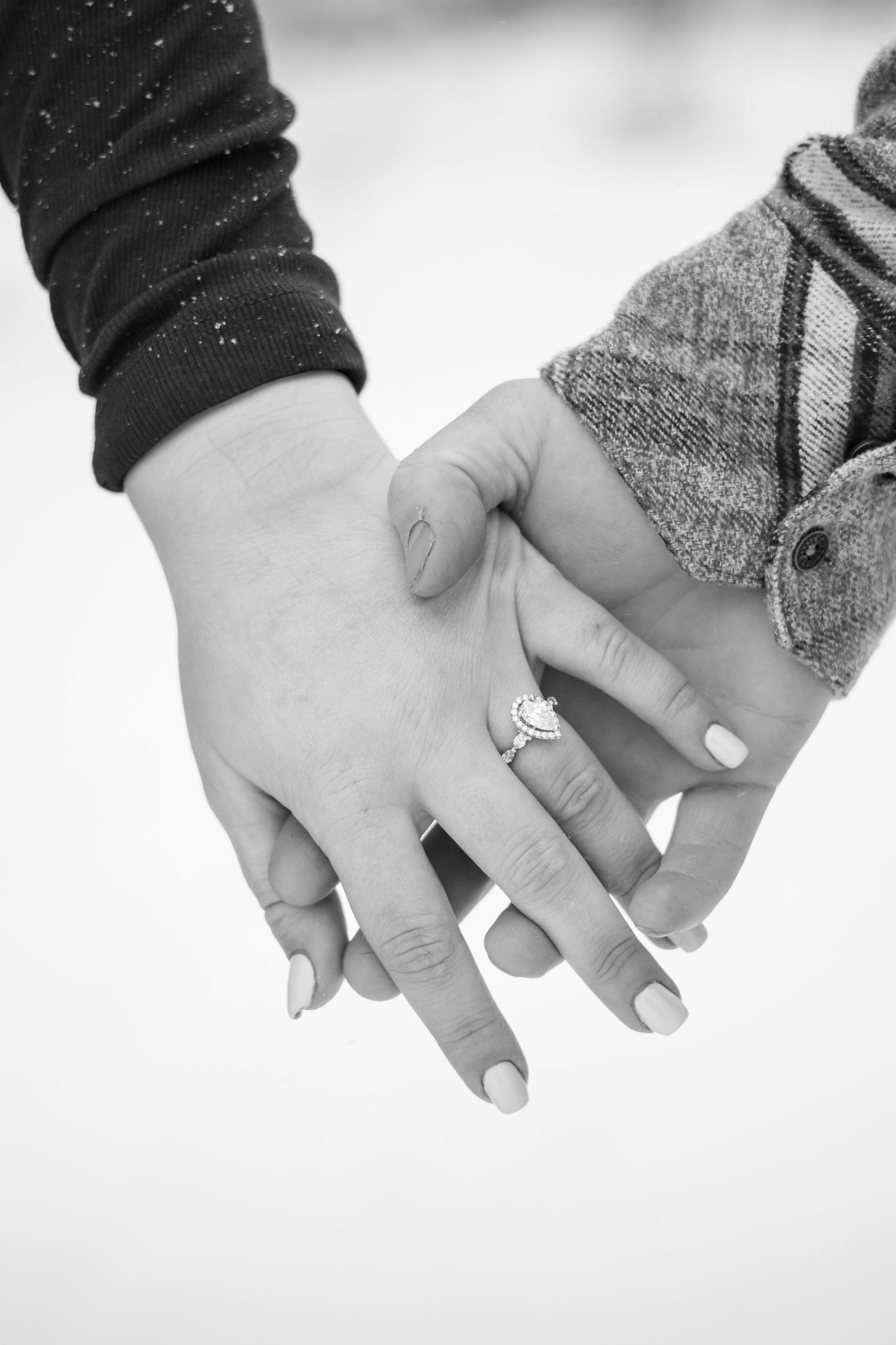 Black and white close-up of two hands with engagement rings touching.