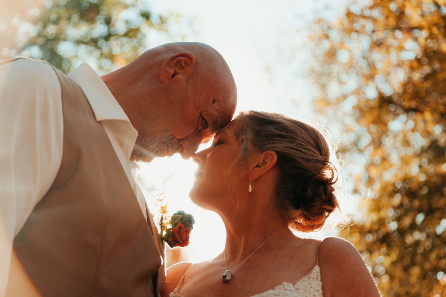 Newly married couple takes a private moment with their foreheads pressed together as the sun shines behind them in the fall in Wisconsin.