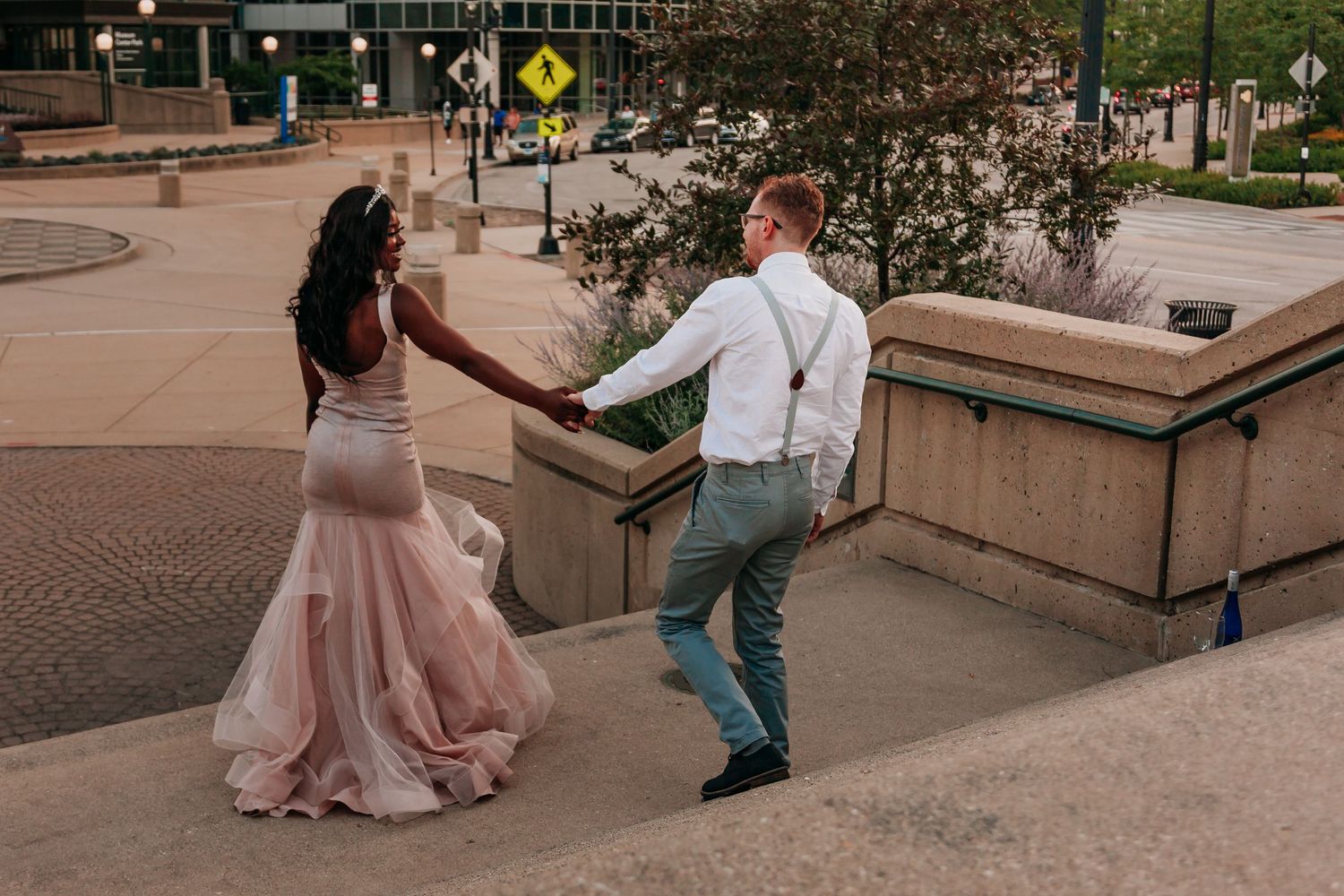 An engaged couple in formalwear walking down a staircase in downtown Milwaukee at sunset.