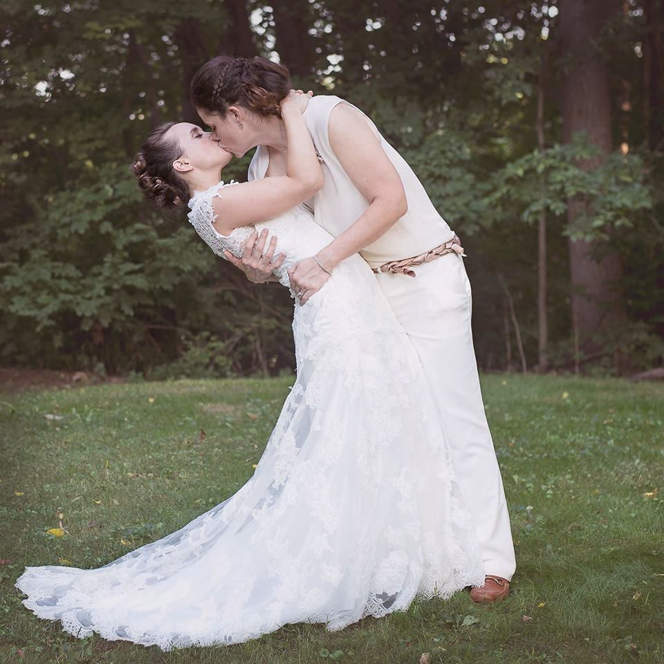 Bride and groom sharing a romantic kiss on green grass in a wooded setting.
