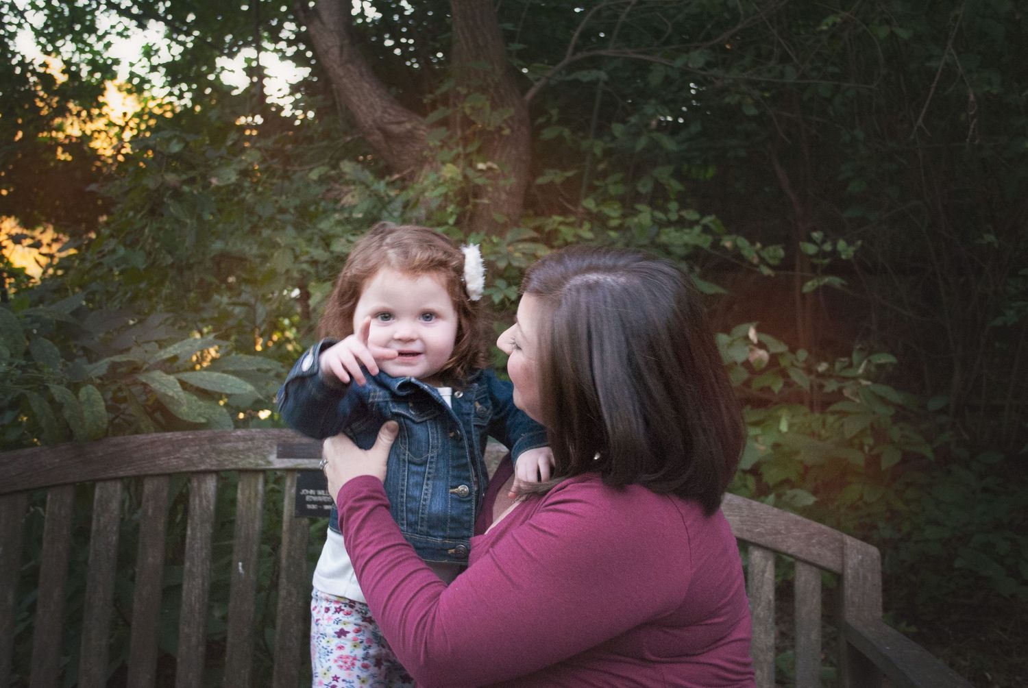 Happy mother lifting and smiling at her adorable toddler daughter in garden.