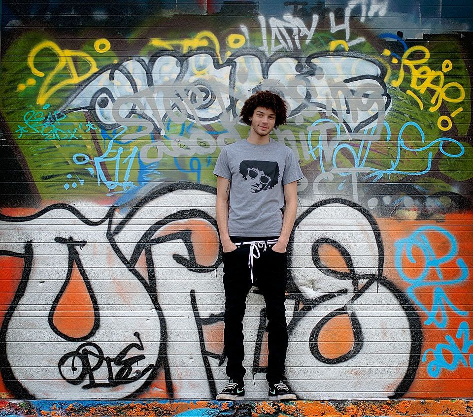 Teenage boy standing in front of colorful urban graffiti wall.