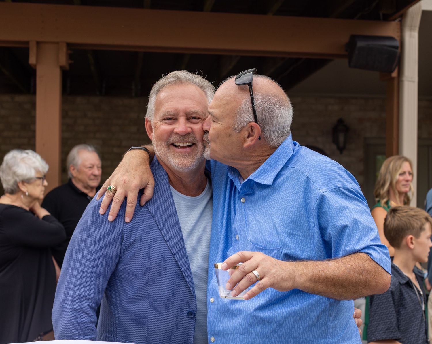 Two men share a joyful embrace and kiss at an outdoor social gathering event.