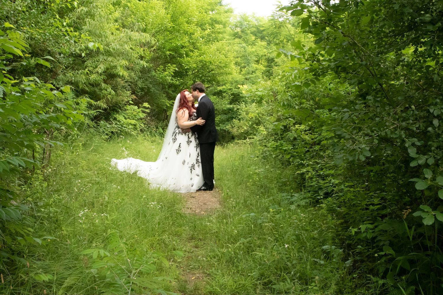 Wedding couple embracing on scenic green forest trail in summer.