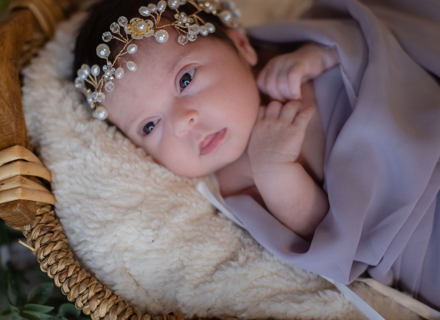Alert newborn baby with pearl headband wrapped in lavender cloth.
