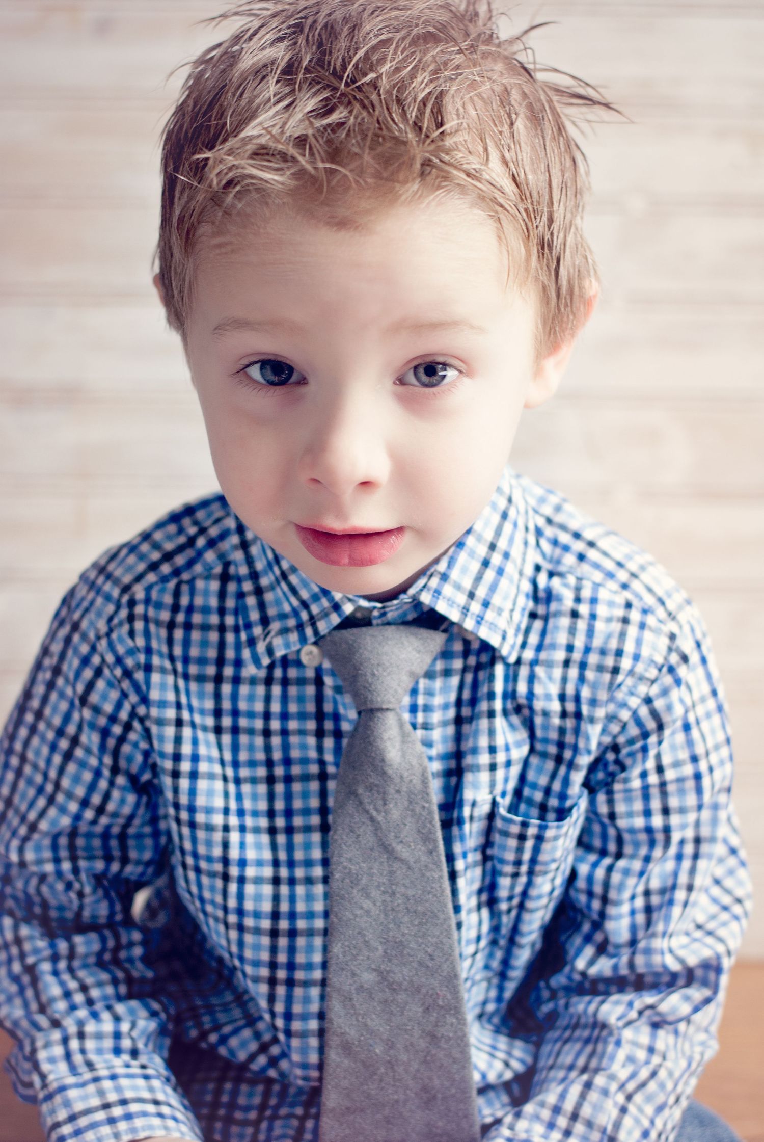 Adorable young boy in blue plaid shirt and gray tie posing for a portrait photo.
