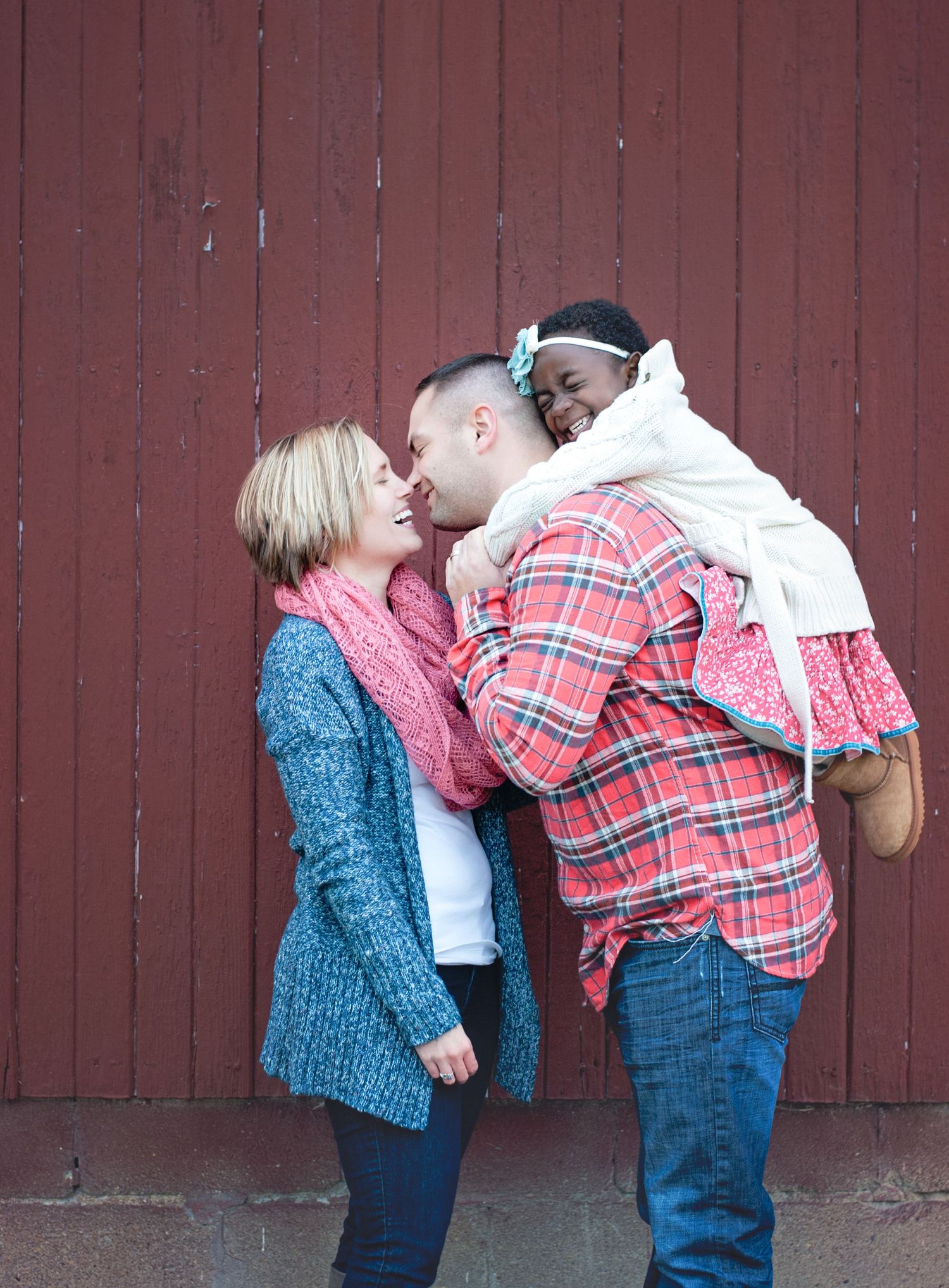 Happy interracial family with mother, father, and young daughter sharing a joyful moment outdoors.