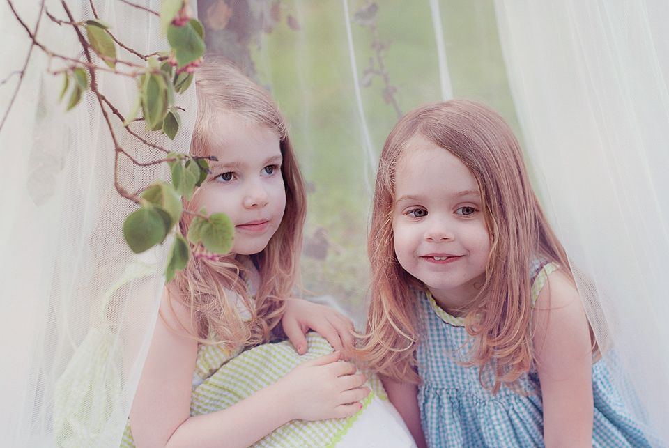 Two young sisters with long hair posing together in soft dreamy portrait photo.