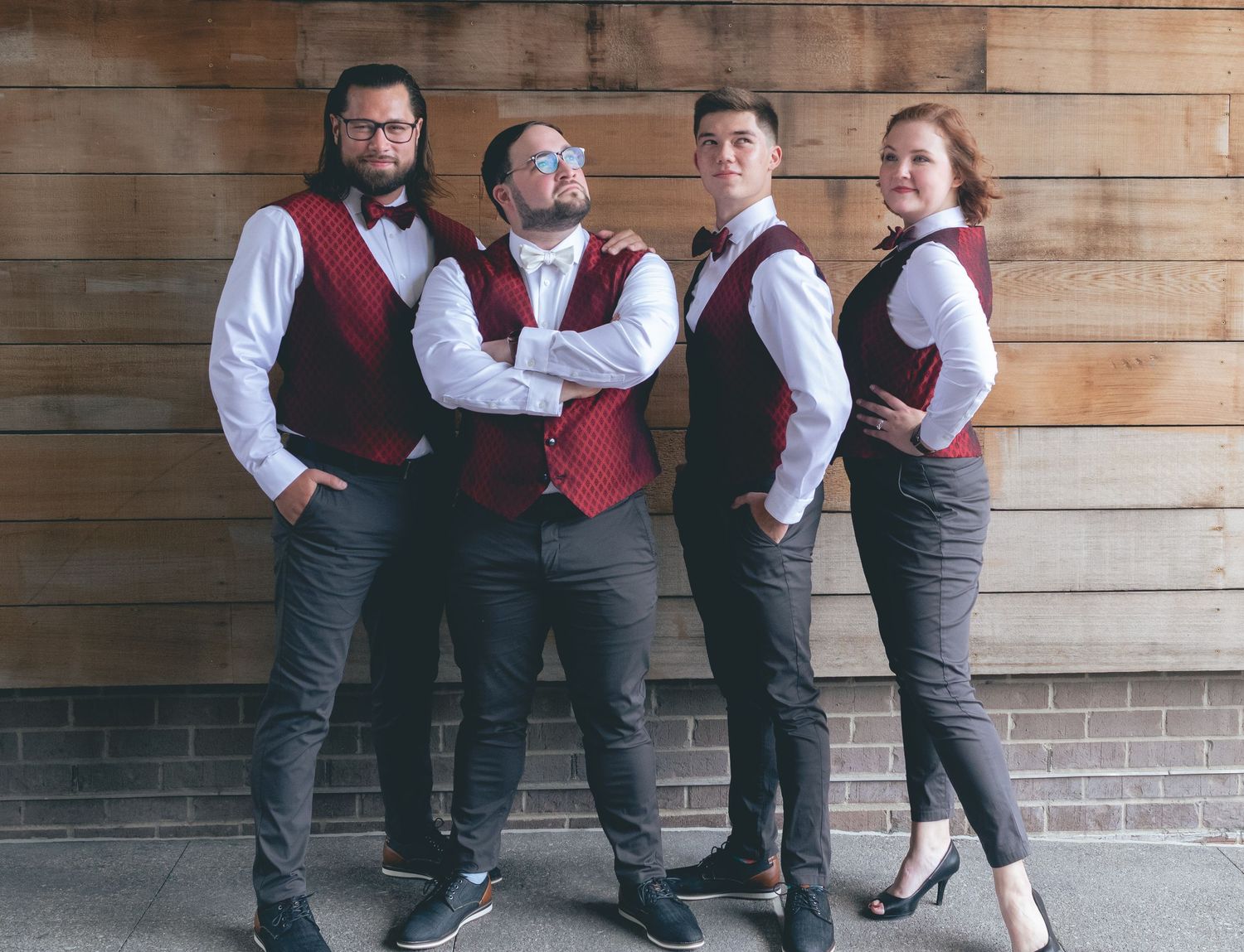 Four people in matching maroon vests and white shirts posing against brick wall.