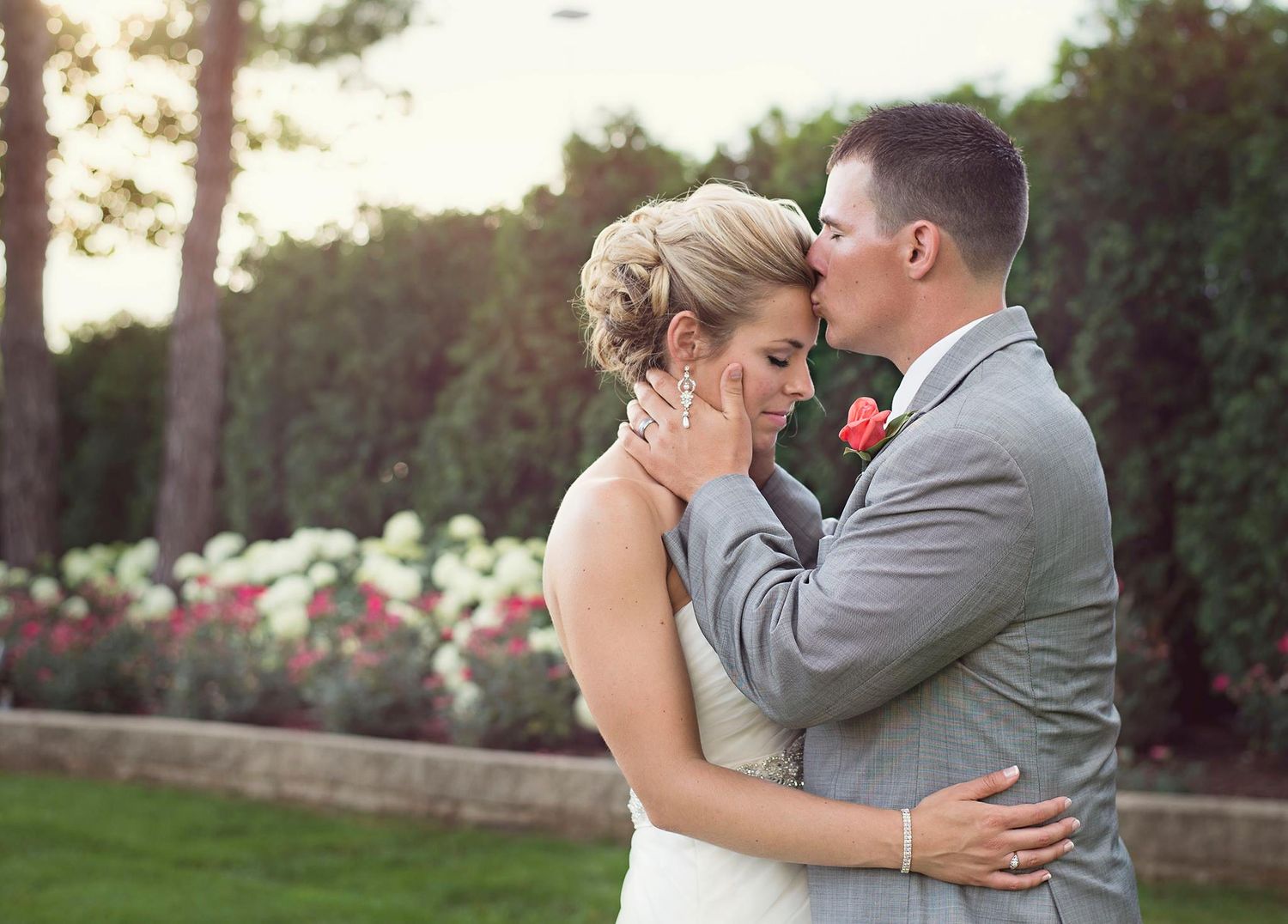 Bride and groom sharing tender moment in garden with pink roses.
