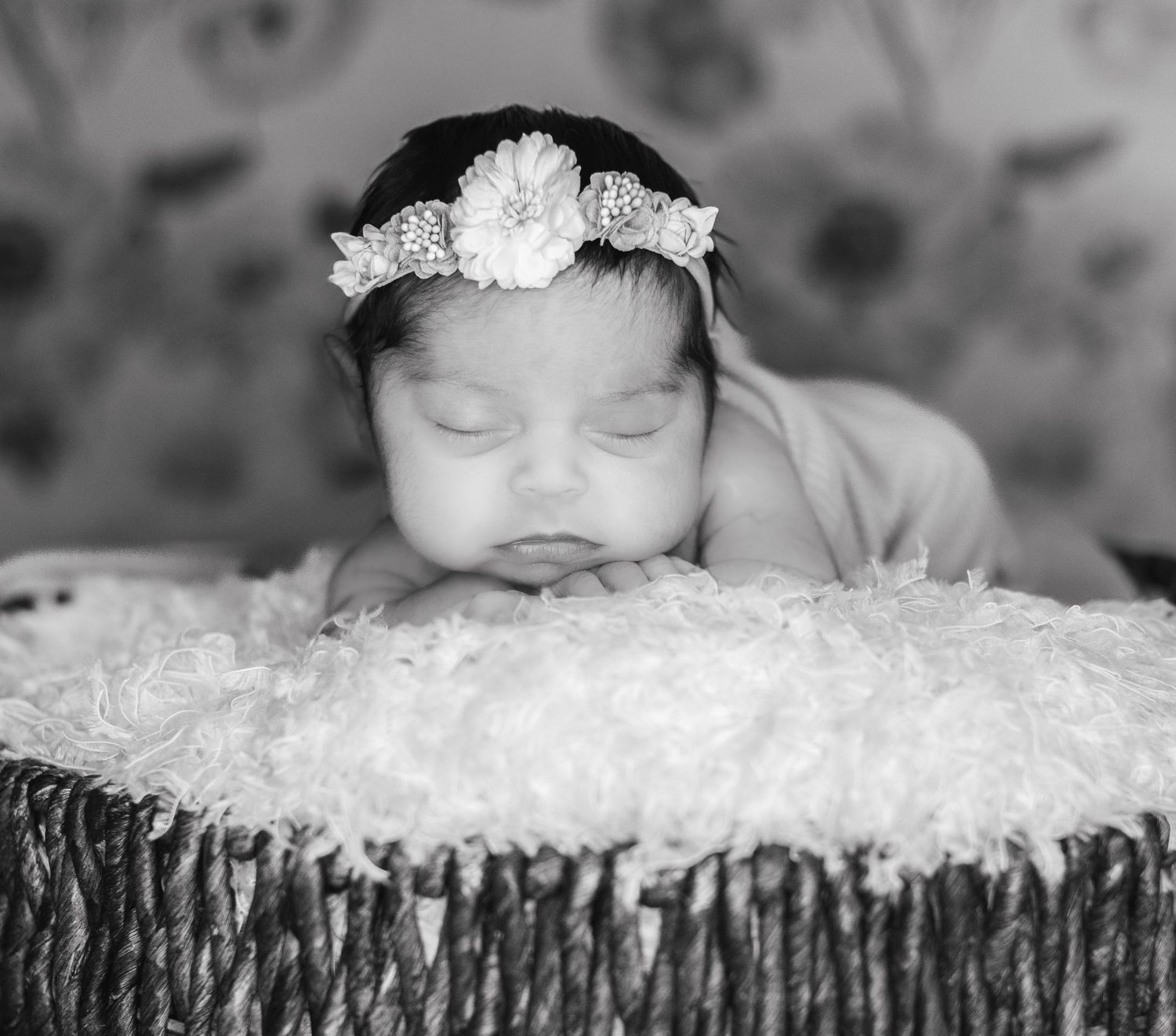 Sleeping newborn baby with flower headband in wicker basket.