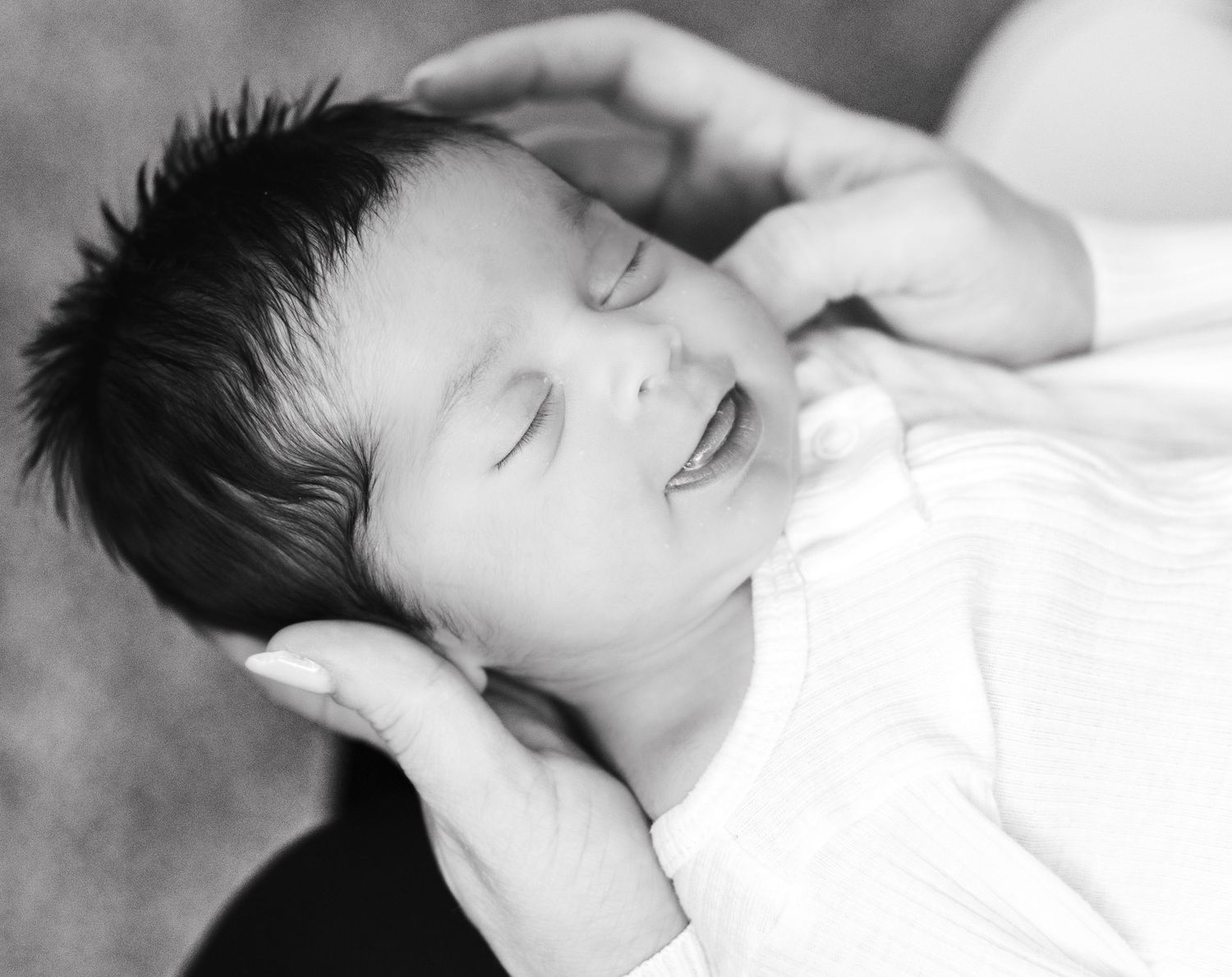 Black and white newborn baby portrait cradled in parents hands.