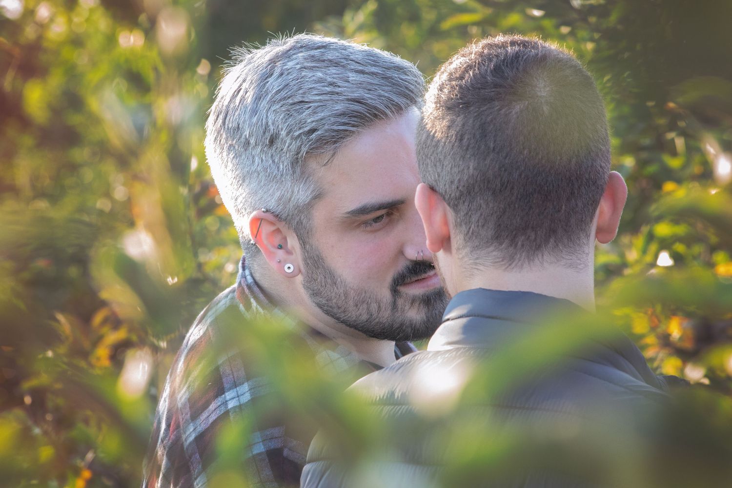 Two men sharing an intimate close moment together outdoors among green foliage.