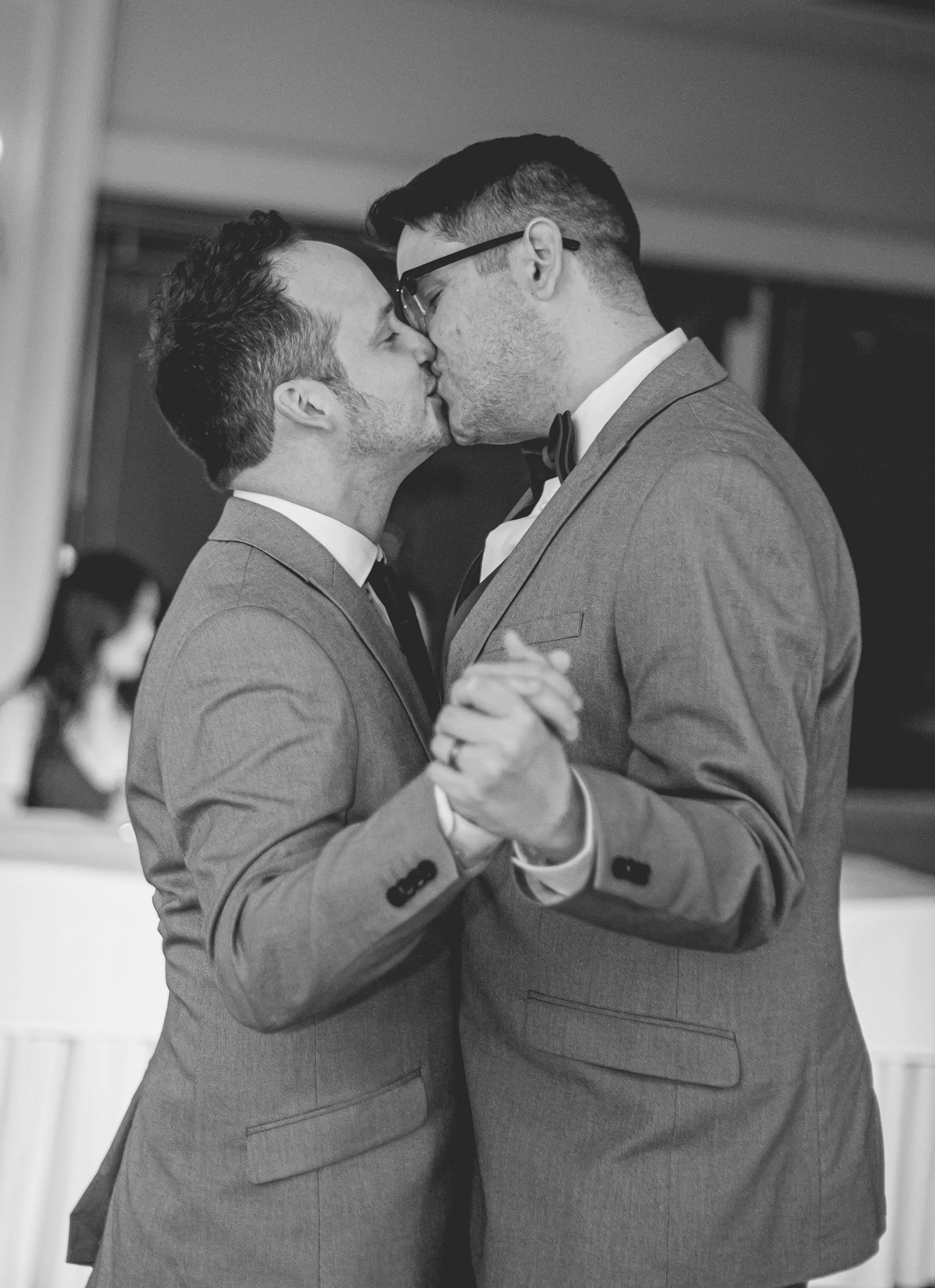 Two grooms sharing first dance kiss in black and white wedding photo.
