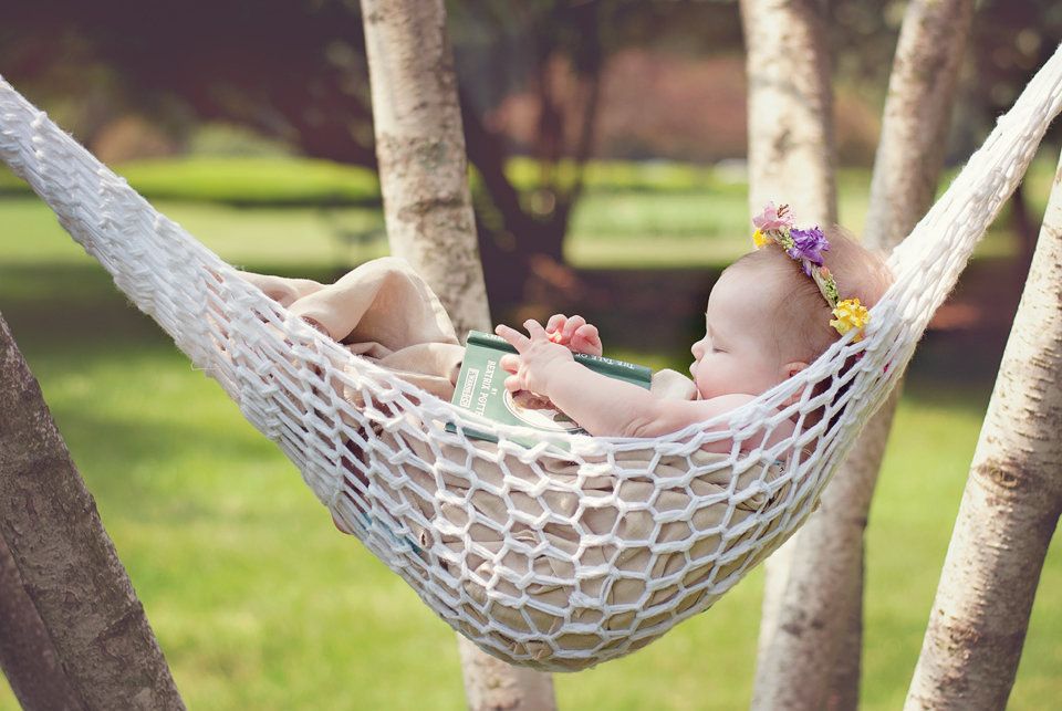 Peaceful baby sleeping in a white rope hammock strung between trees in a sunny garden.
