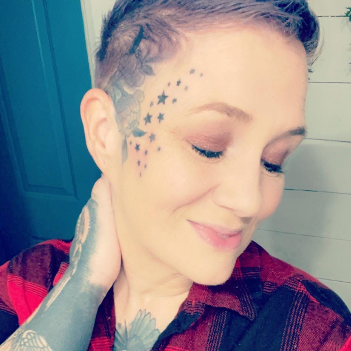 Woman with star face tattoos and shaved sides hairstyle wearing red flannel shirt.