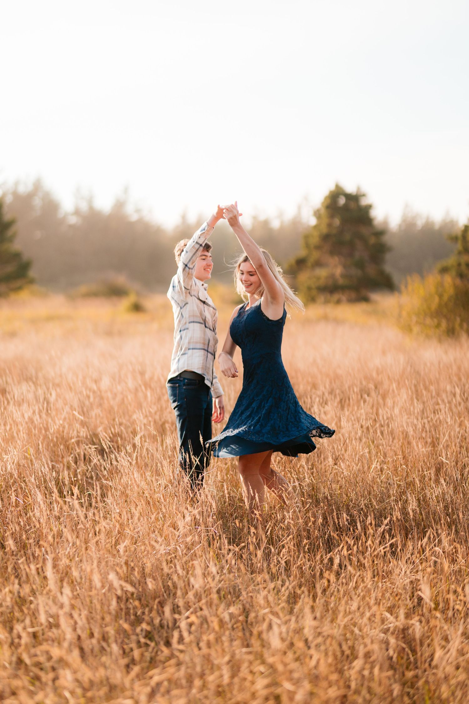Young couple dancing and holding hands in a golden sunlit field at sunset.