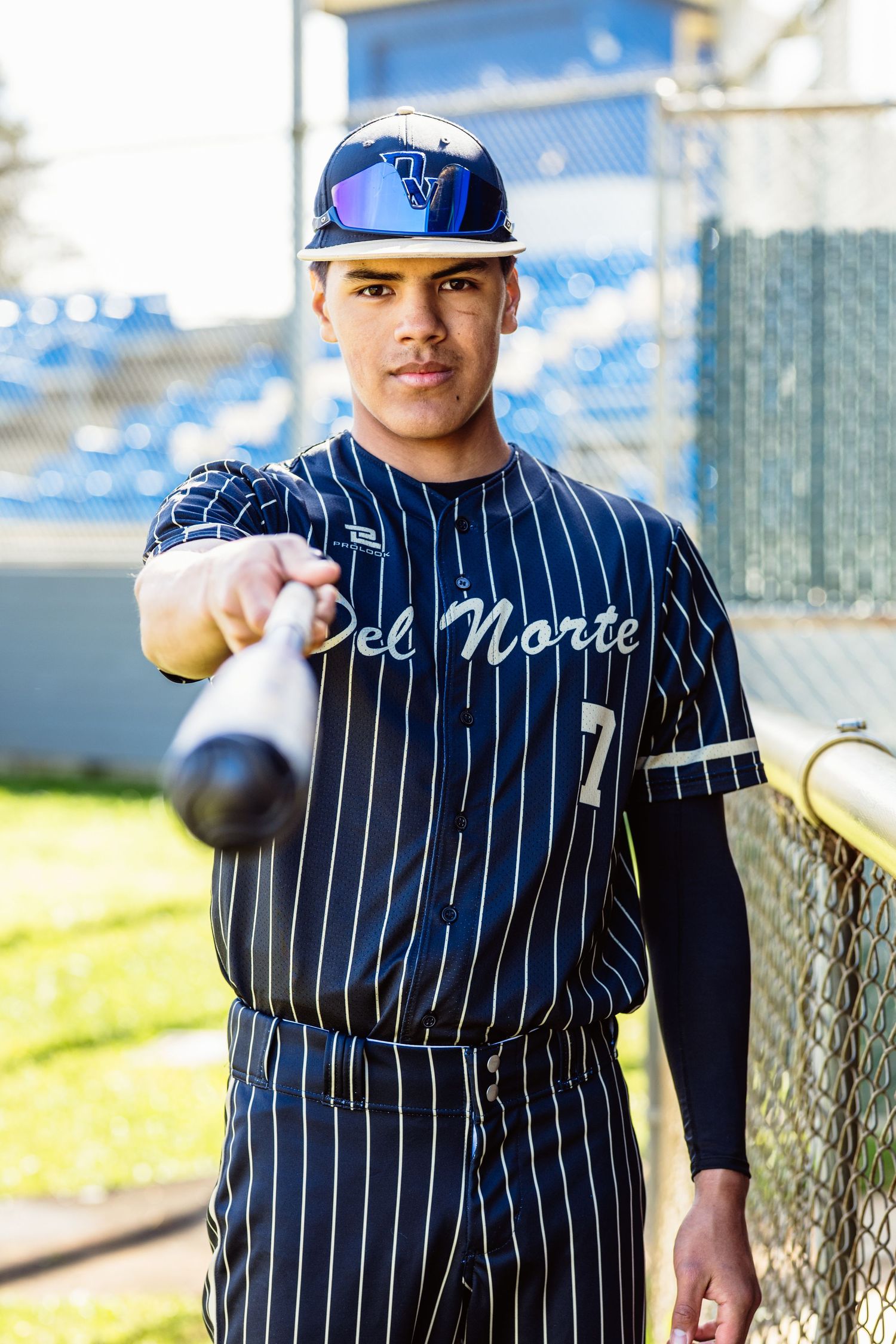 Del Norte baseball player #7 points bat toward camera in stadium.