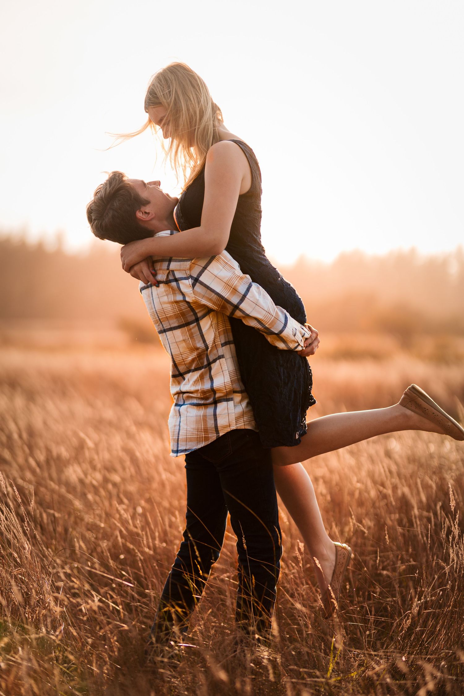 Young man lifting his girlfriend joyfully in a glowing sunlit field at golden hour.