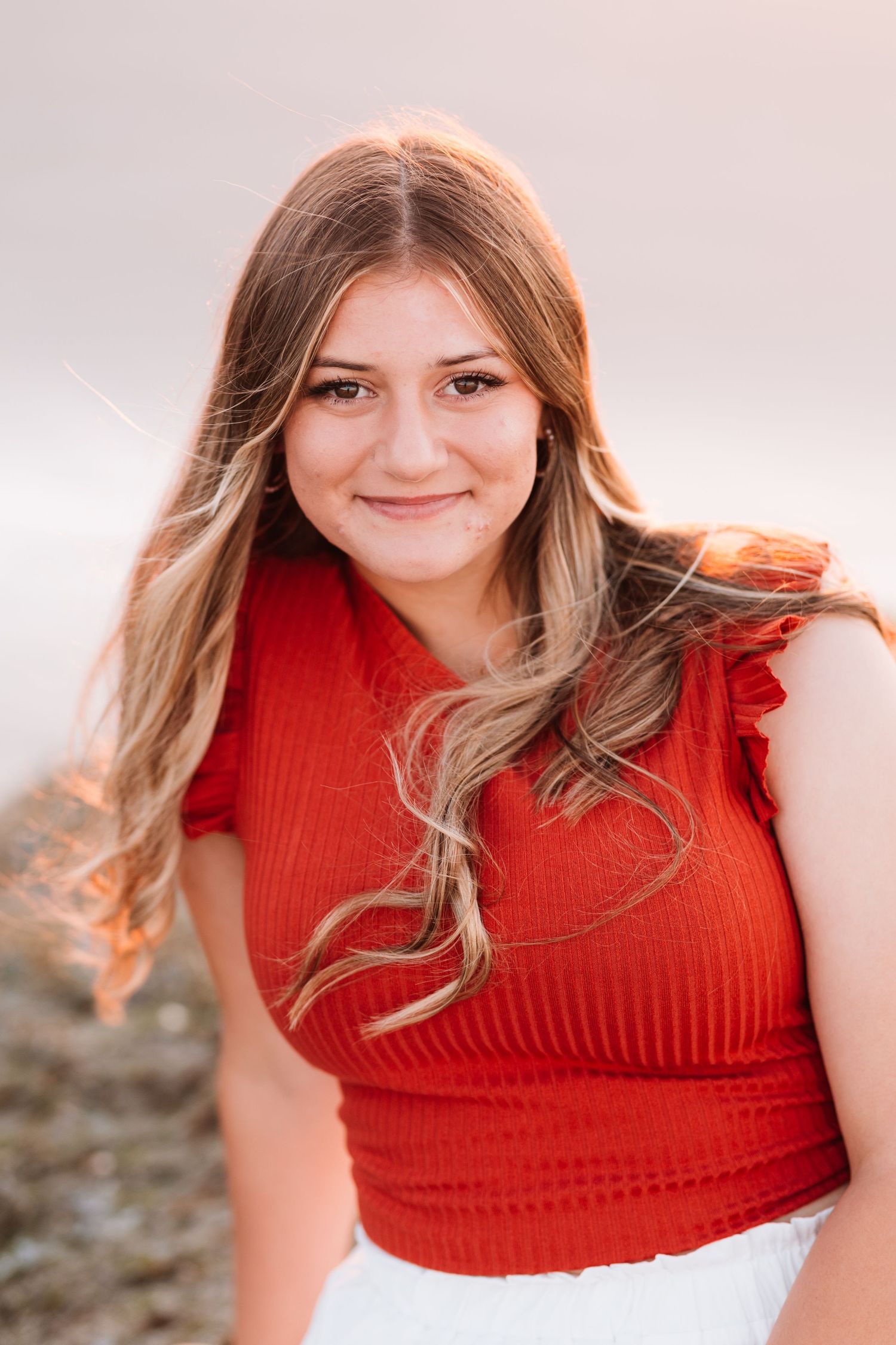 Close-up portrait of smiling teen girl in red ruffled top with long wavy blonde hair outdoors.