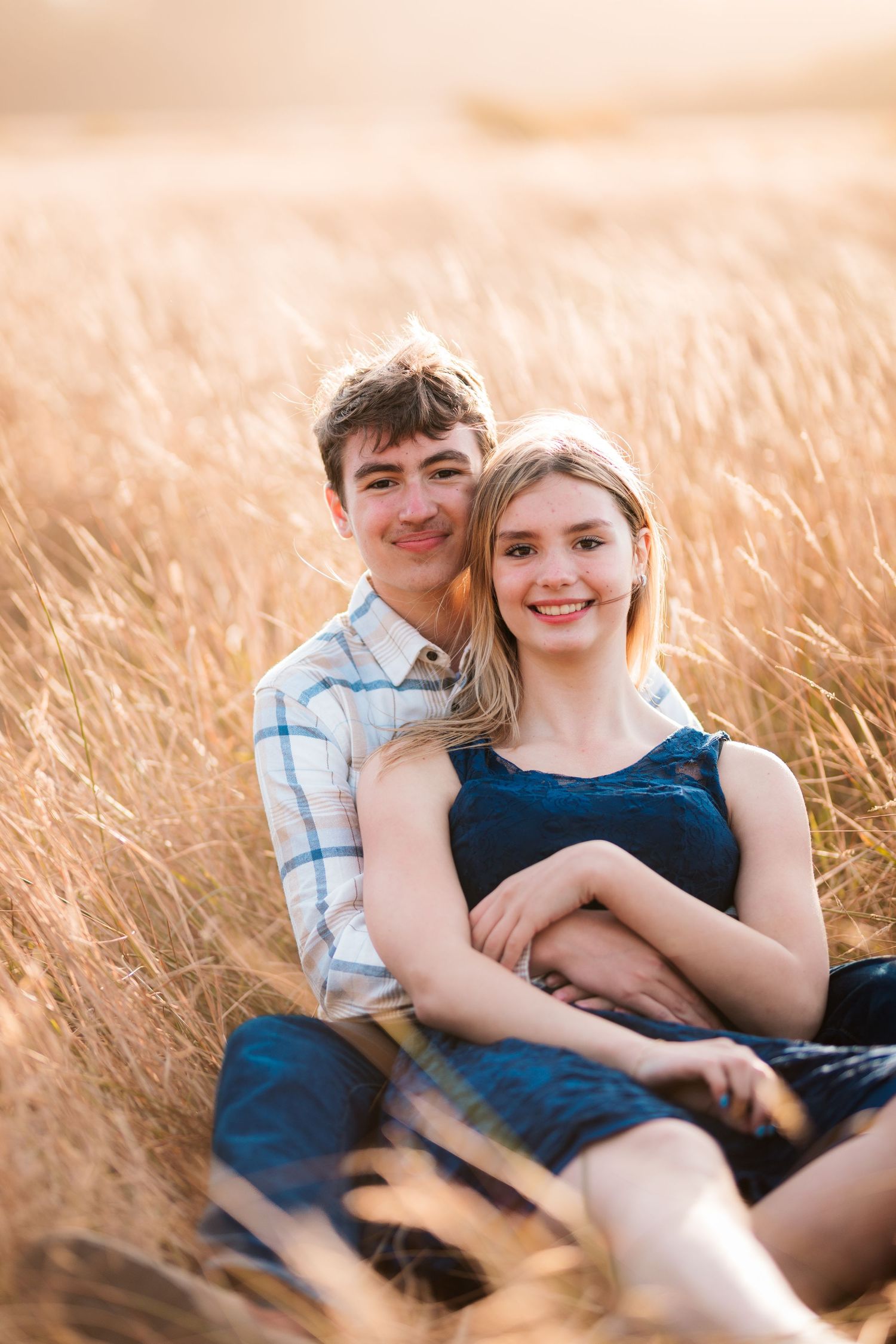 Young couple cuddling together and smiling in a beautiful golden sunlit meadow.