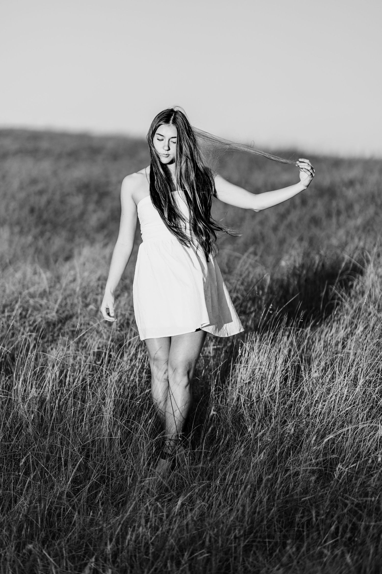 Black and white photo of a young woman in a white dress walking through a grassy field.