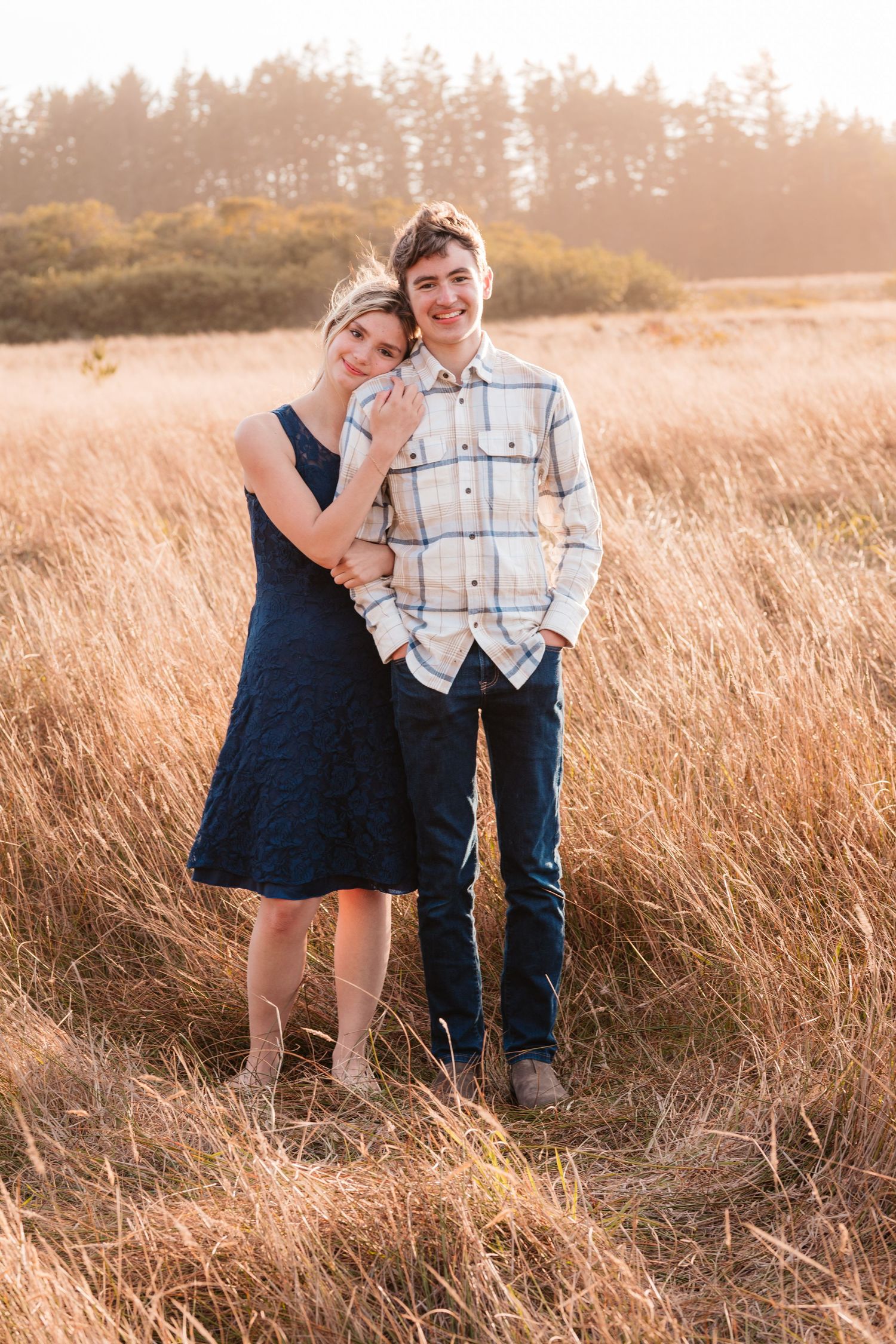 Young couple standing close together smiling in a golden field at sunset.