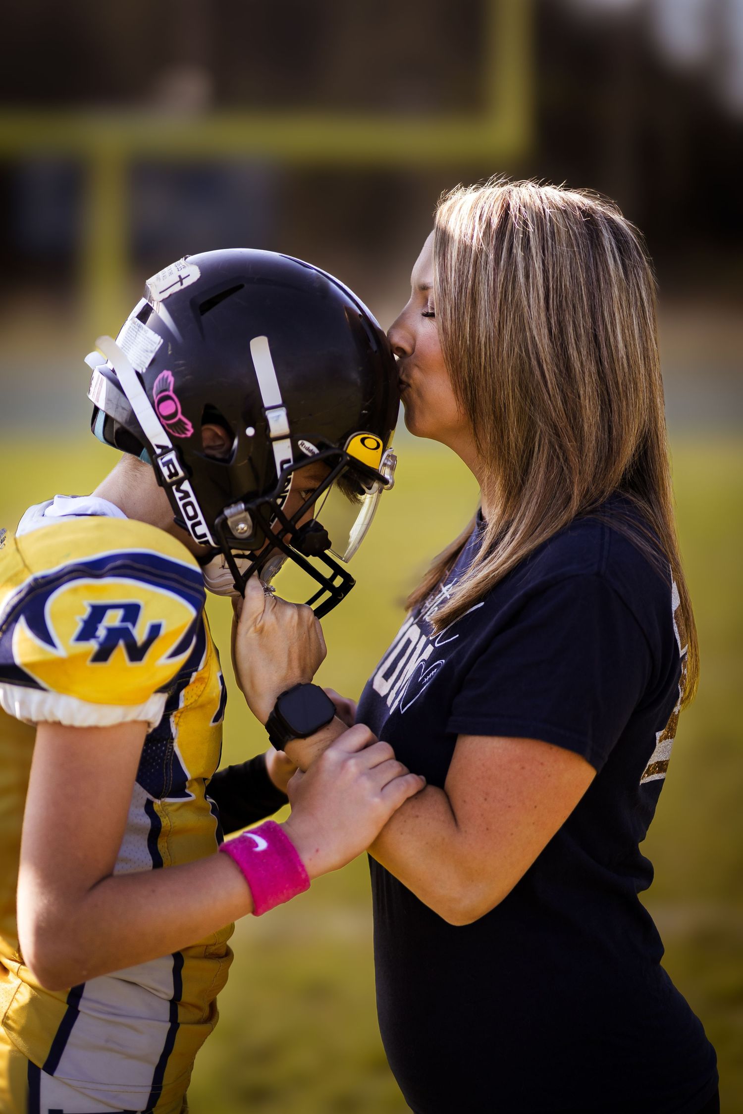 Woman kissing football player wearing helmet in yellow and blue uniform on field.
