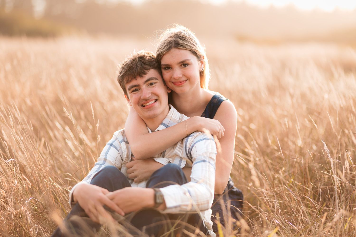 Young couple sitting together smiling warmly in a sun-drenched golden grass field.